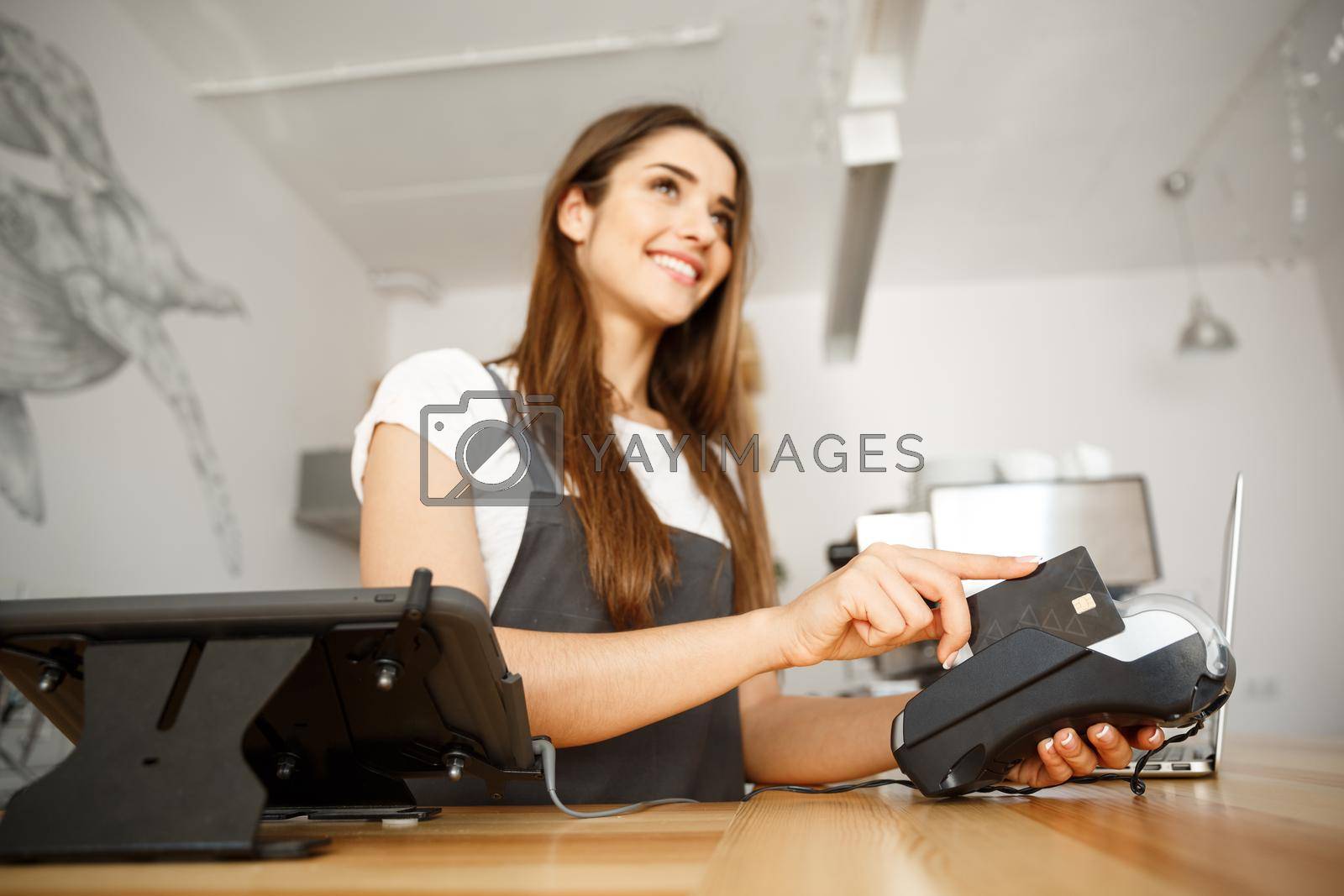 Royalty free image of Coffee Business Concept - Beautiful female barista giving payment service for customer with credit card and smiling while working at the bar counter in modern coffee shop. by Benzoix