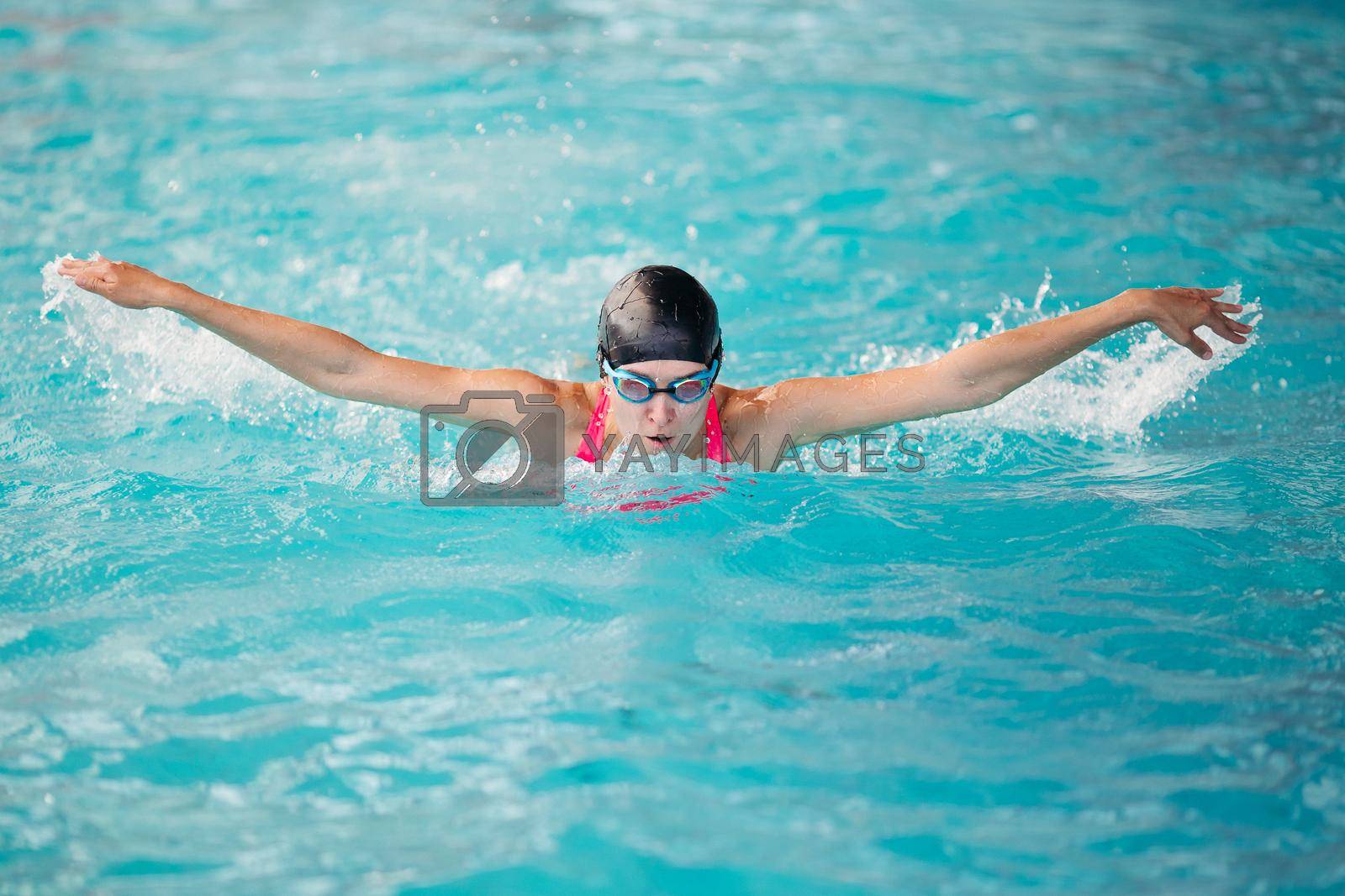 Royalty free image of Young girl swimming butterfly stroke style in the blue water poo by StudioLucky