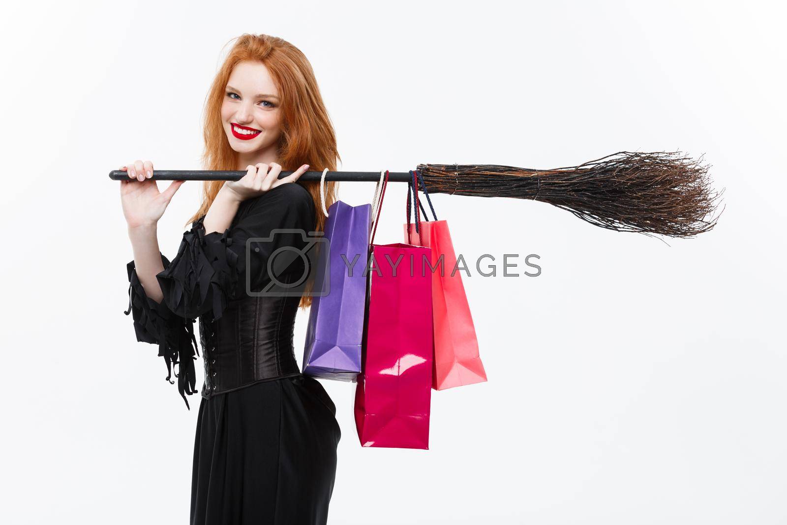 Royalty free image of Halloween witch concept - Happy Halloween Witch smiling and holding colorful shopping bags on white background. by Benzoix