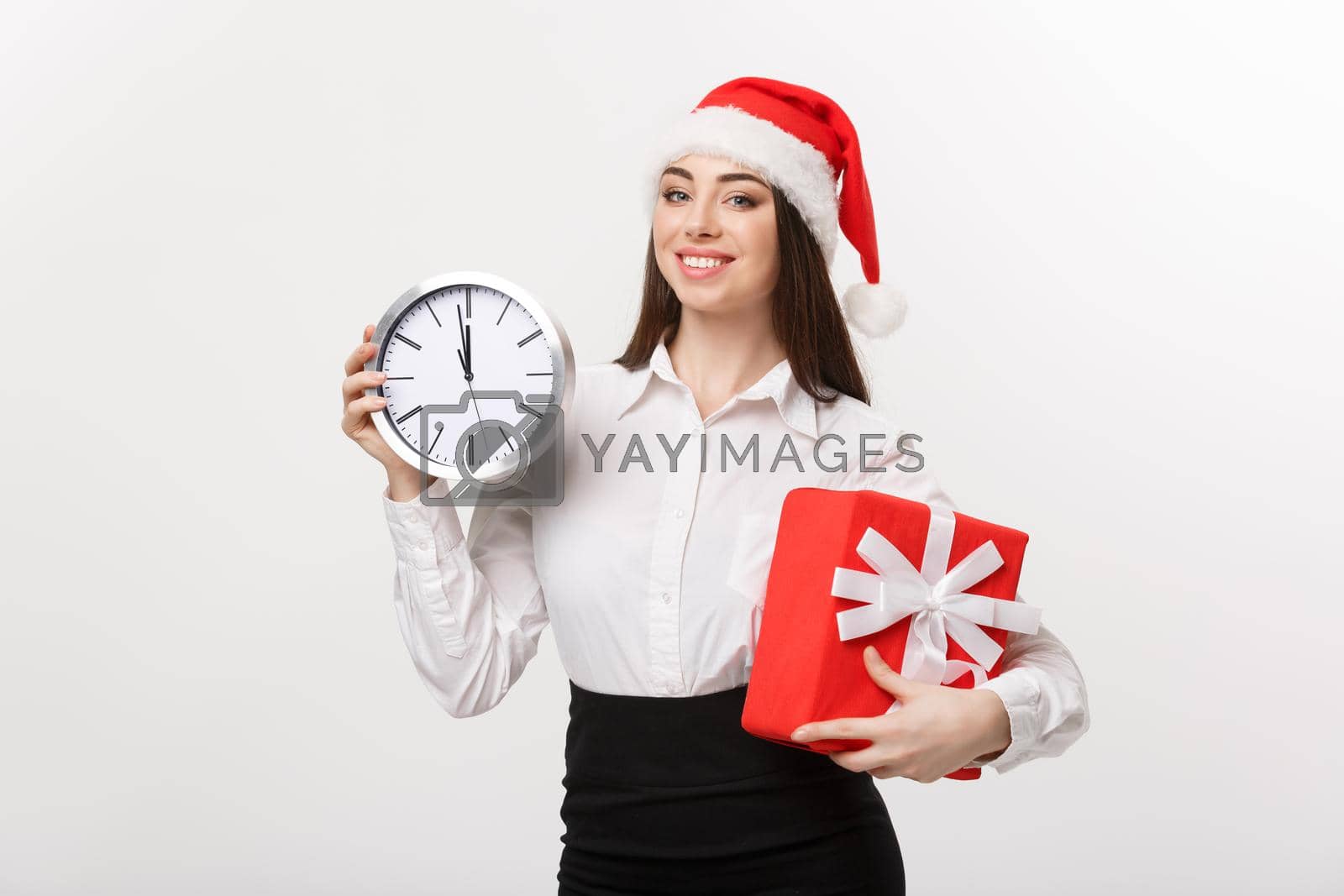 Royalty free image of Time management concept - Young business woman with santa hat holding a clock and present isolated over white background. by Benzoix