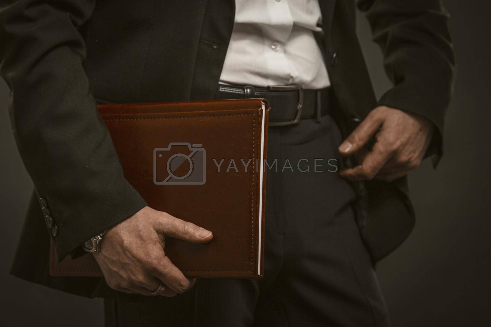 Royalty free image of Successful businessman holds documents folder. Good looking caucasian man in formal wear holding brown leather document folder. Close up shot. Paperwork concept. Toned image by LipikStockMedia