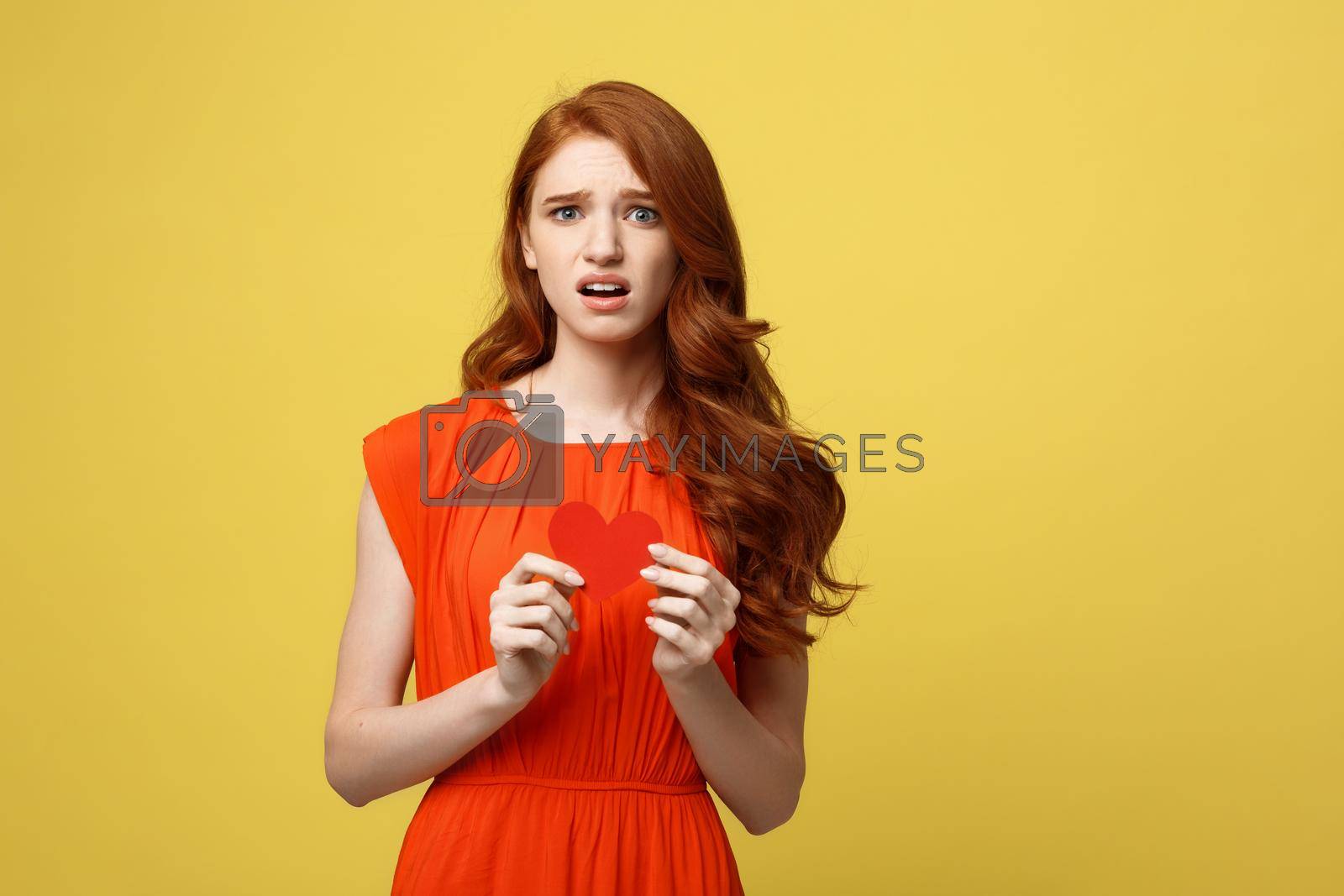 Royalty free image of Attractive ginger girl holding paper heart and frowning, being nervous while confessing to her crush by Benzoix