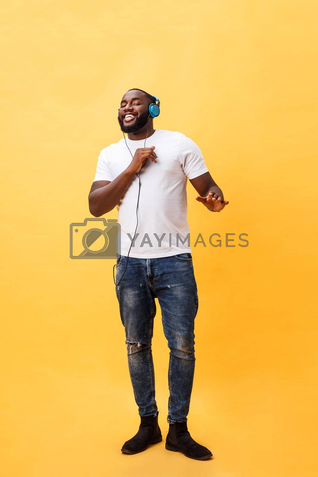 Royalty free image of Full length portrait of a cherry young african american man listening to music with headphones and dancing isolated over yellow background by Benzoix