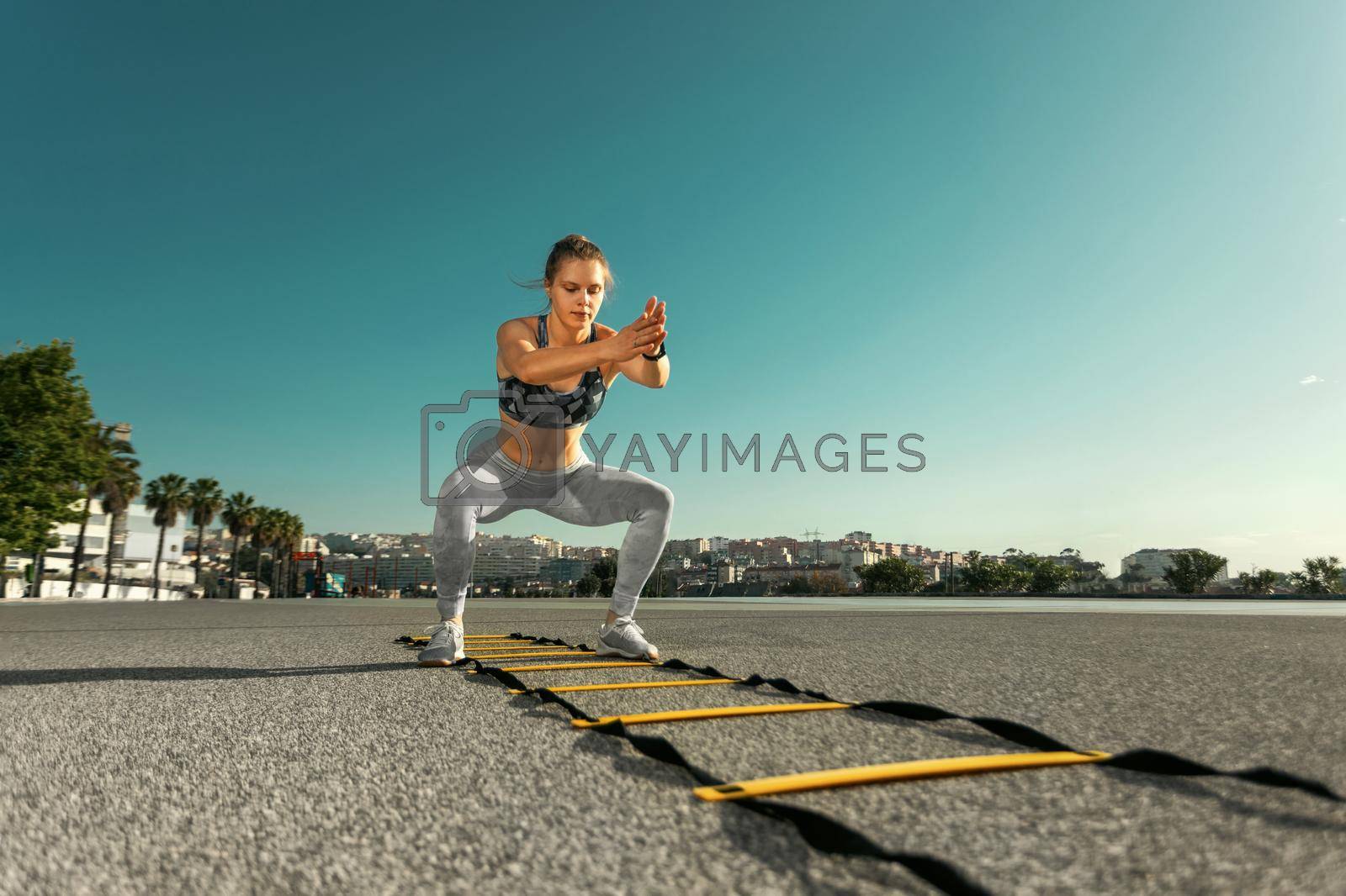 Royalty free image of Young sportswoman training jumping on an agility ladder coordinating outdoors by MikeOrlov