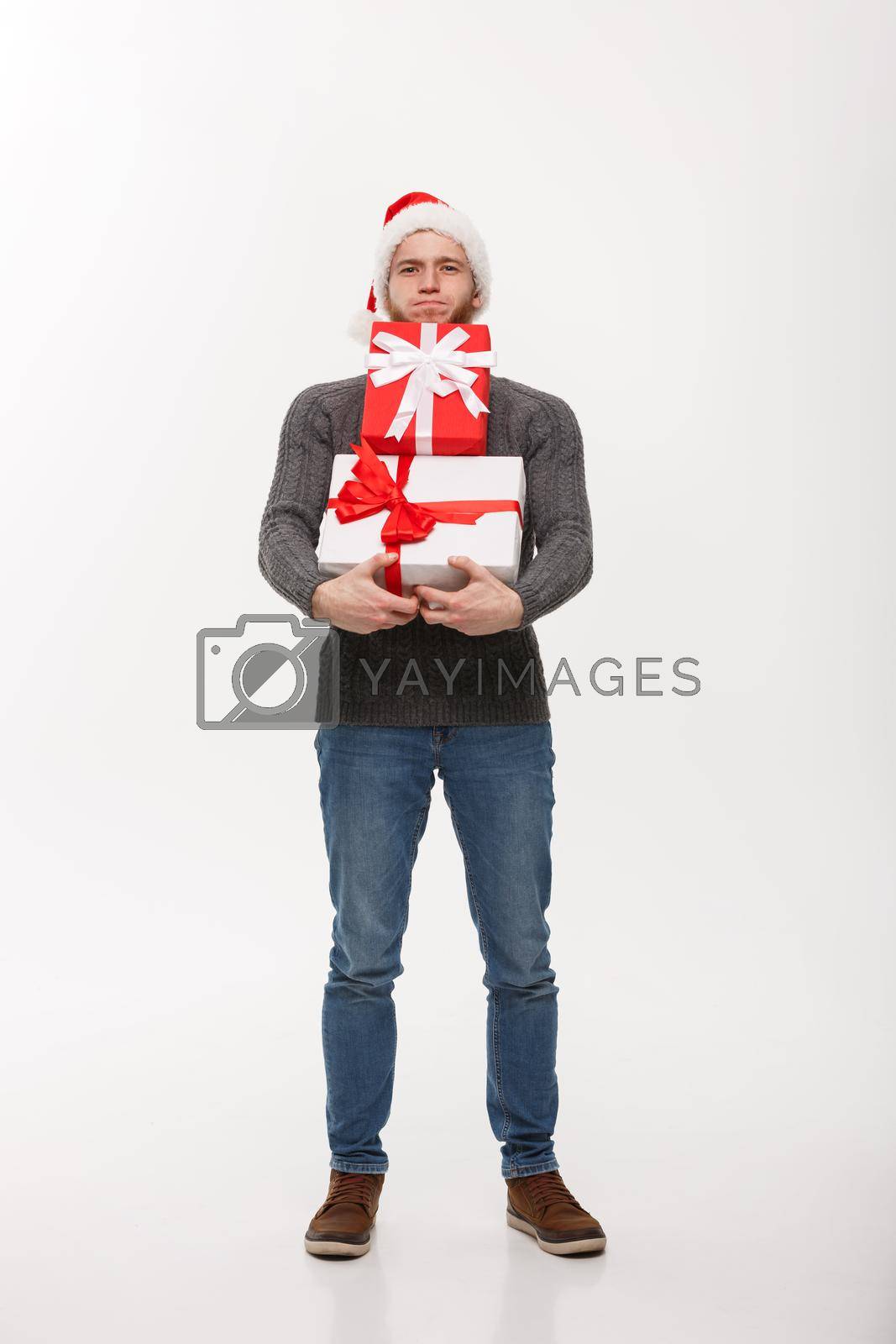 Royalty free image of Christmas Concept - young handsome man with beard holding heavy presents with exhausted facial expression on white background. by Benzoix
