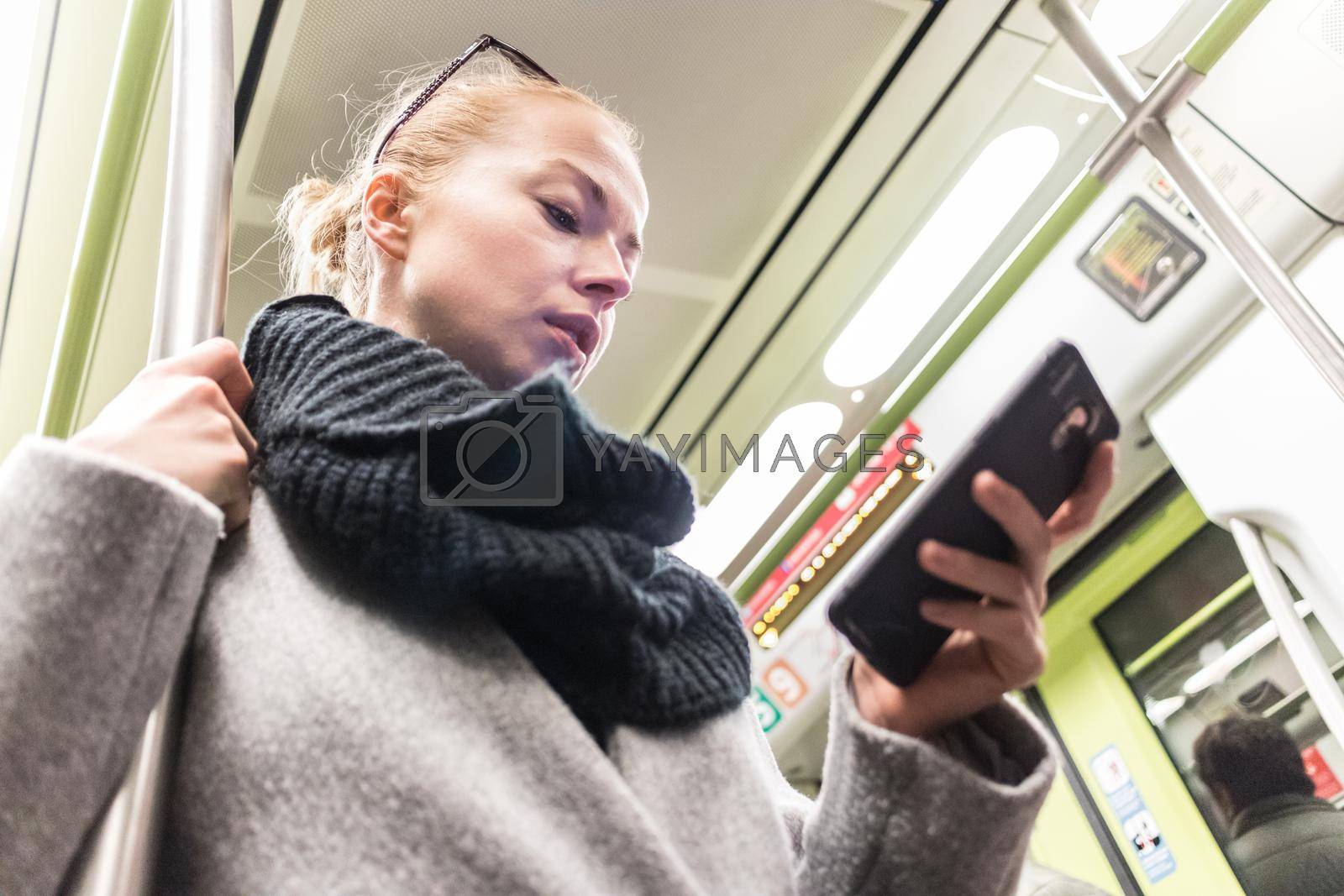 Young woman passenger using smartphone while moving in the modern metro, commuting by public transport.