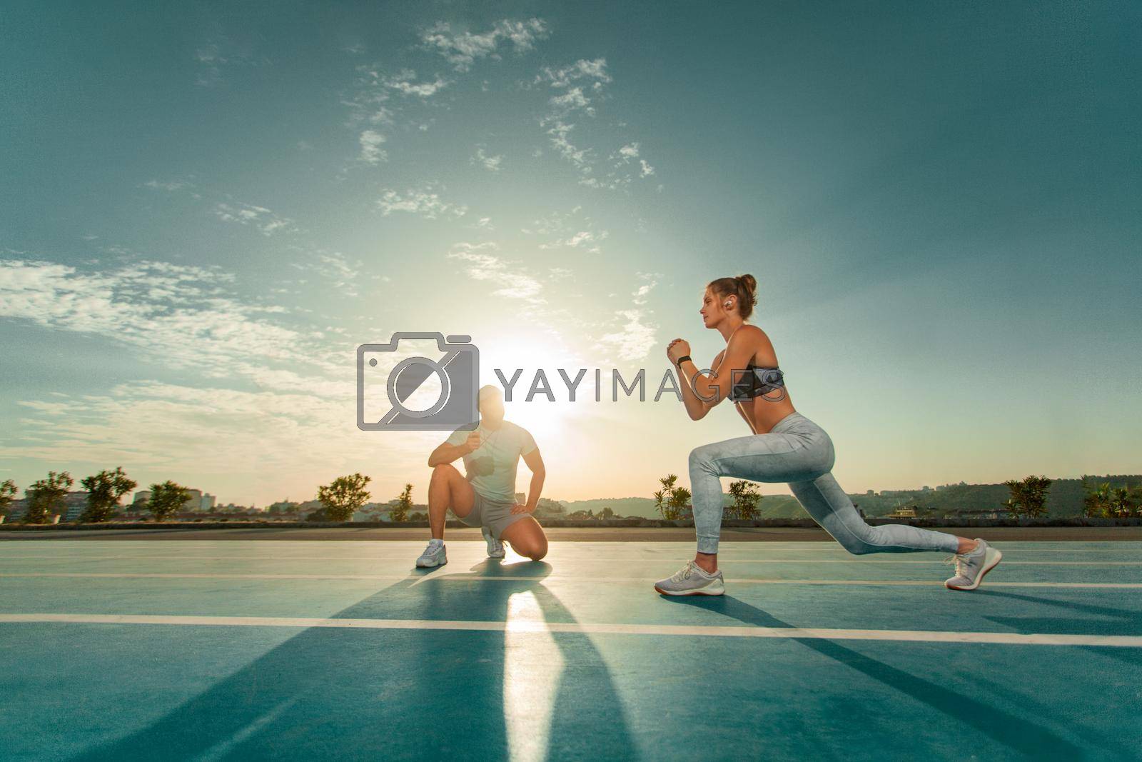 Royalty free image of Instructor and athlete runner on the track. The athletics marks the time in the lunges exercise on a stopwatch. Fitness trainer and mentee. by MikeOrlov