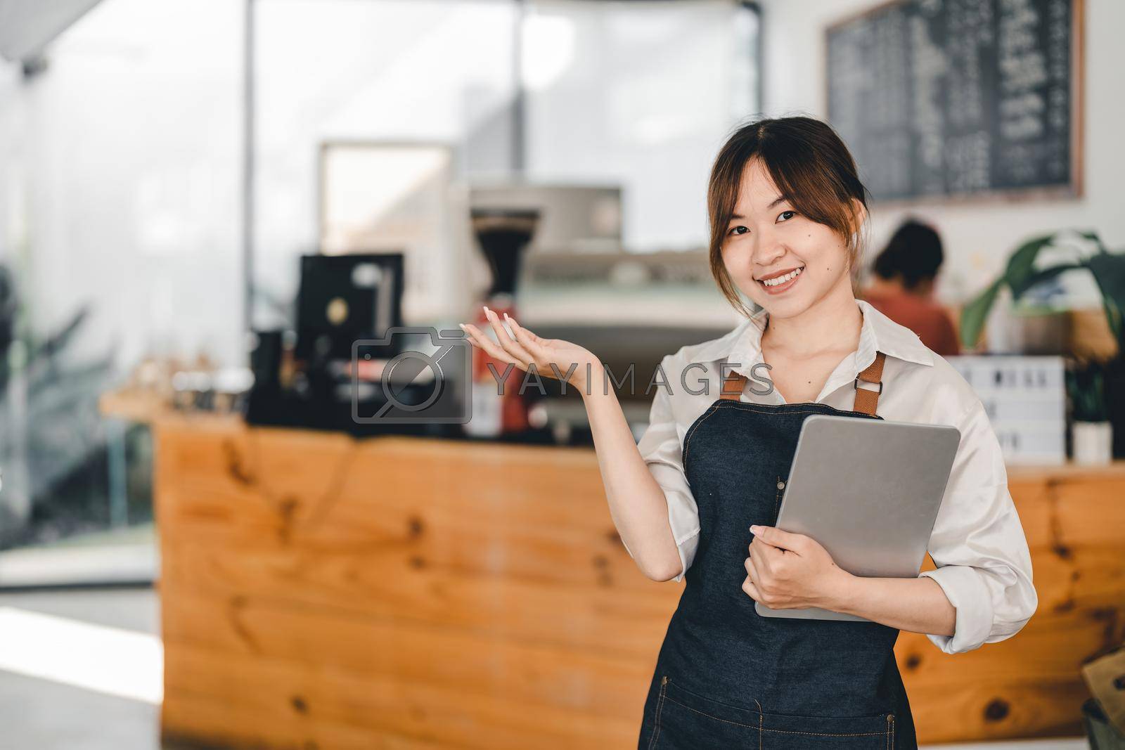 Royalty free image of Asian woman barista holding digital tablet for checking order from customer at coffee cafe shop background , SME business concept by nateemee