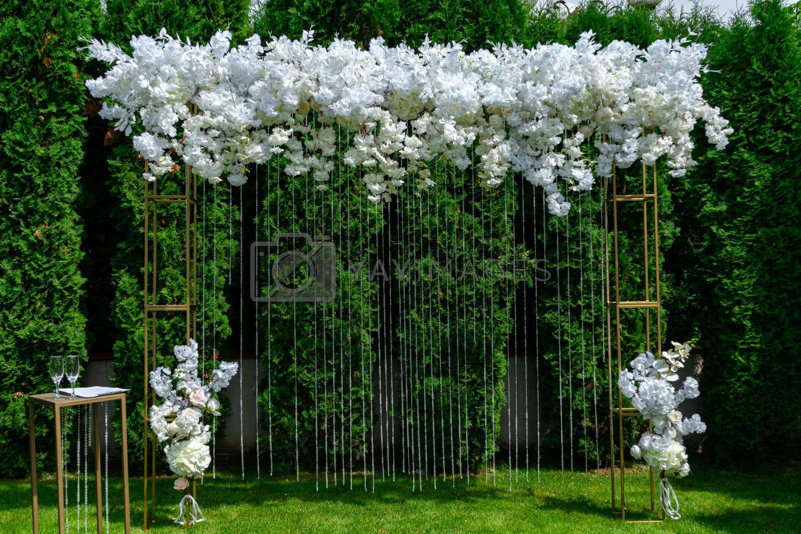 Royalty free image of White wedding arch on a background of evergreen thuja. Summer wedding ceremony in the park by Serhii_Voroshchuk