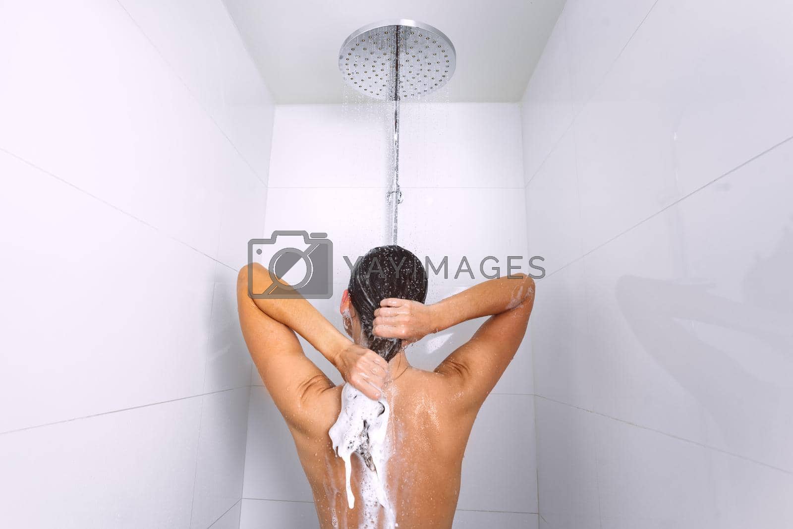 Royalty free image of Rear view of young woman taking shower and washing hair with shampoo under water falling from rain shower head by DariaKulkova