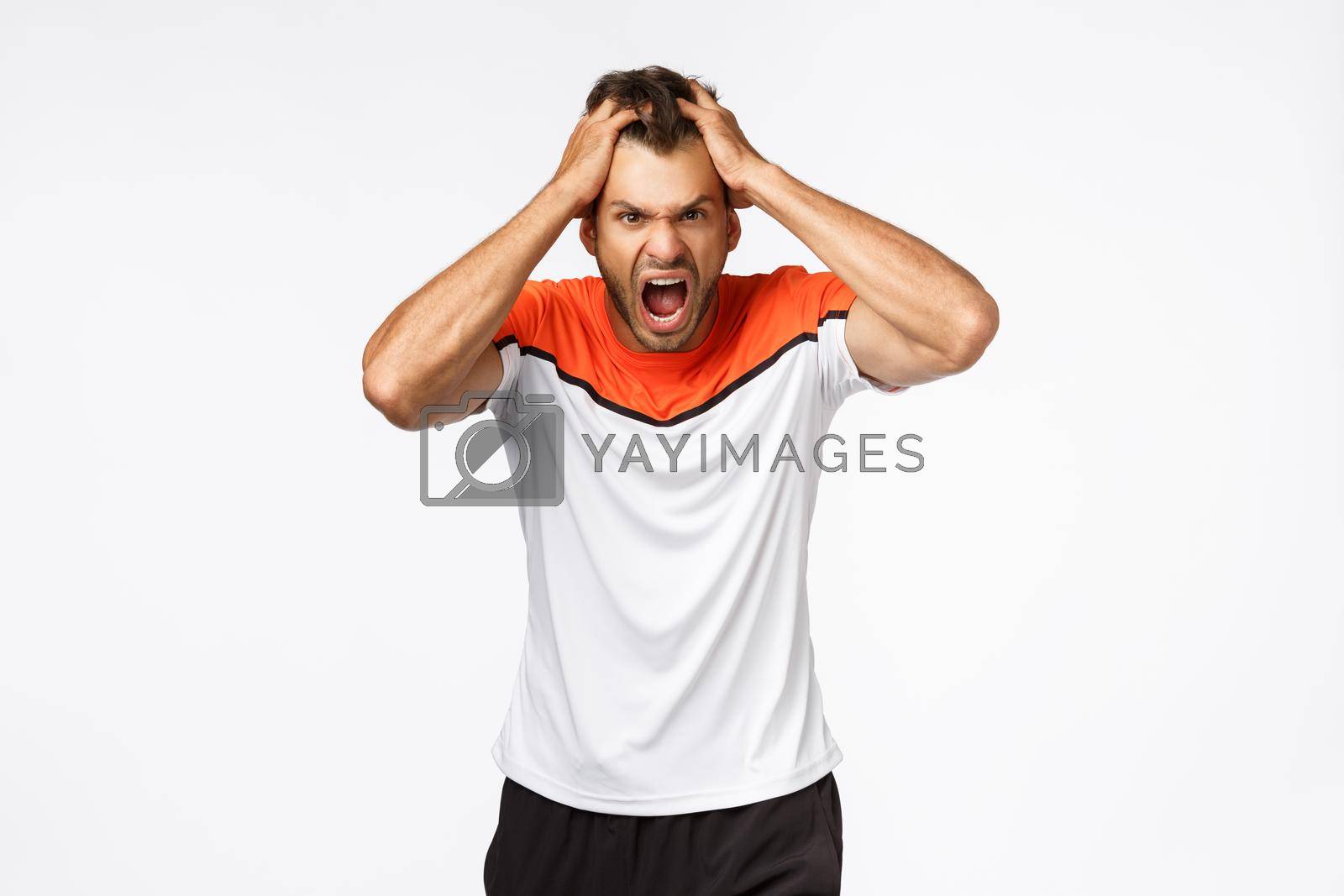 Royalty free image of Angry, aggressive mascular sportsman looking furious, grab head in rage and fury, shouting and grimacing from anger and disappointment. Athlete lost match, team scored goal, white background by Benzoix