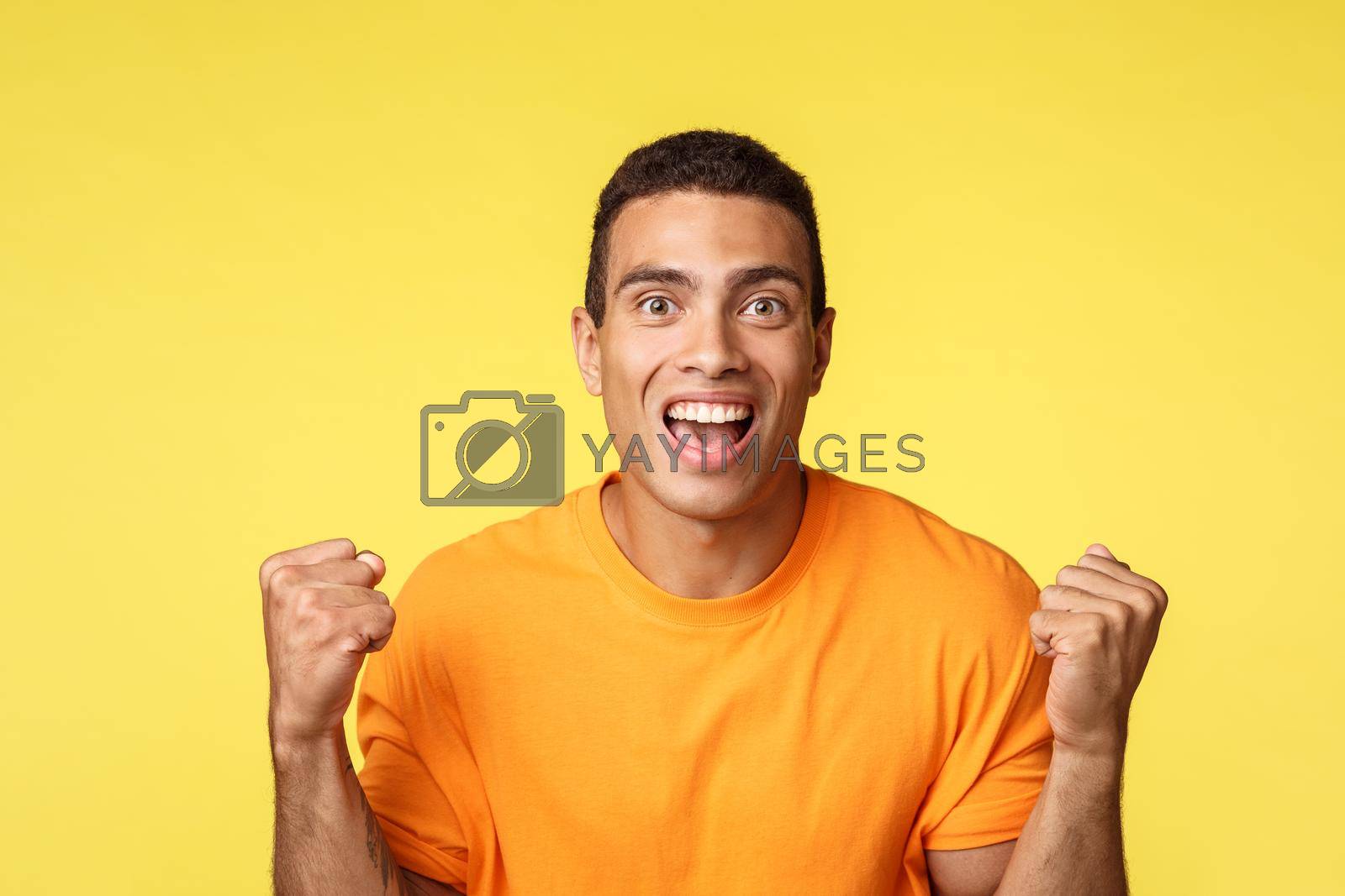 Achievement, celebration and win concept. Handsome relieved cheerful young man clench hands, fist pump and smiling become winner or champion, receive prize, achieve success, yellow background.
