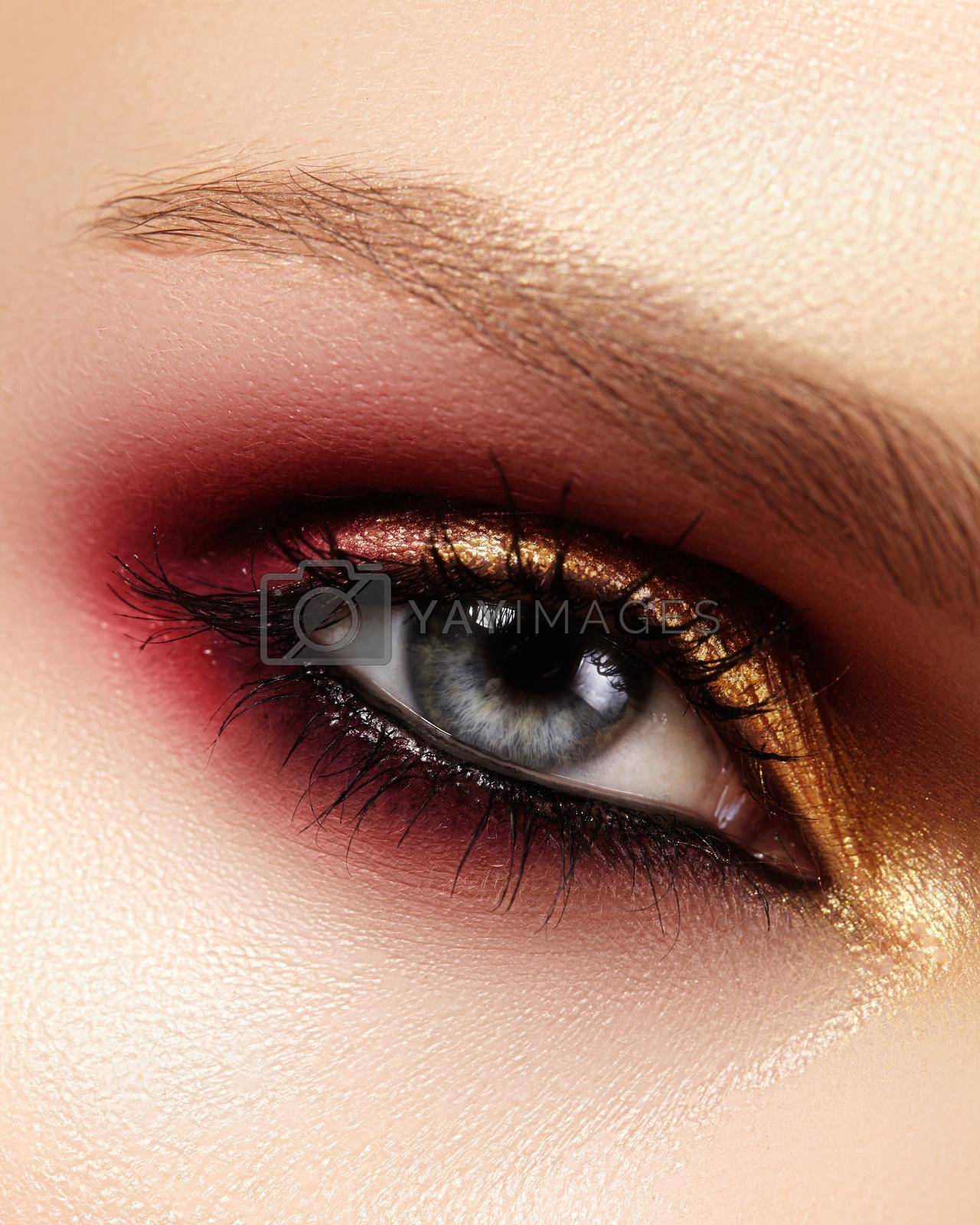 Royalty free image of Closeup female eye with fashion bright make-up. Beautiful gold, red eyeshadow, glitter, black eyeliner. Shape Eyebrows by MarinaFrost