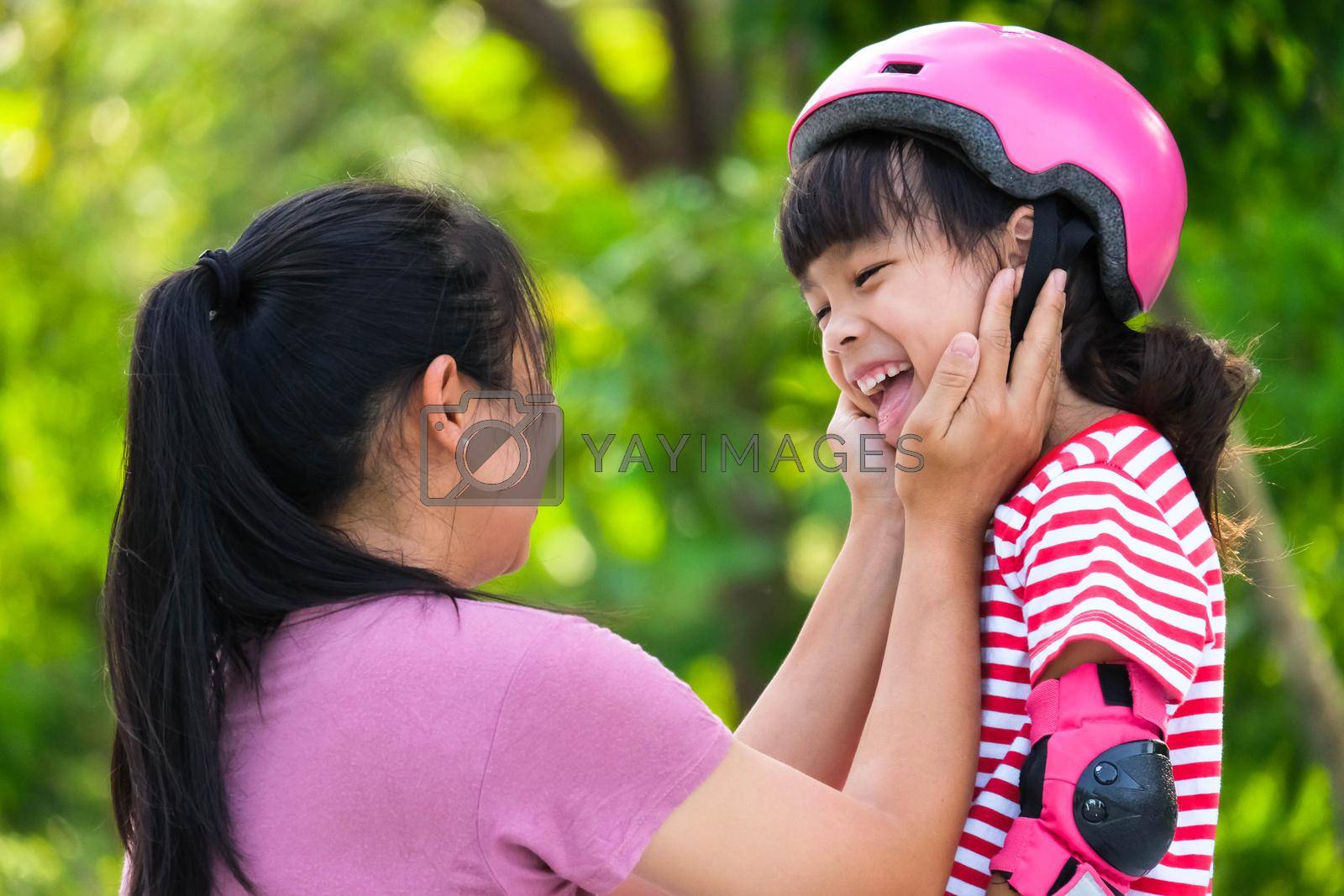 Royalty free image of Asian mother helps daughter put on protective pads and safety helmet before practicing roller skating in the park. Exciting outdoor activities for kids. by TEERASAK