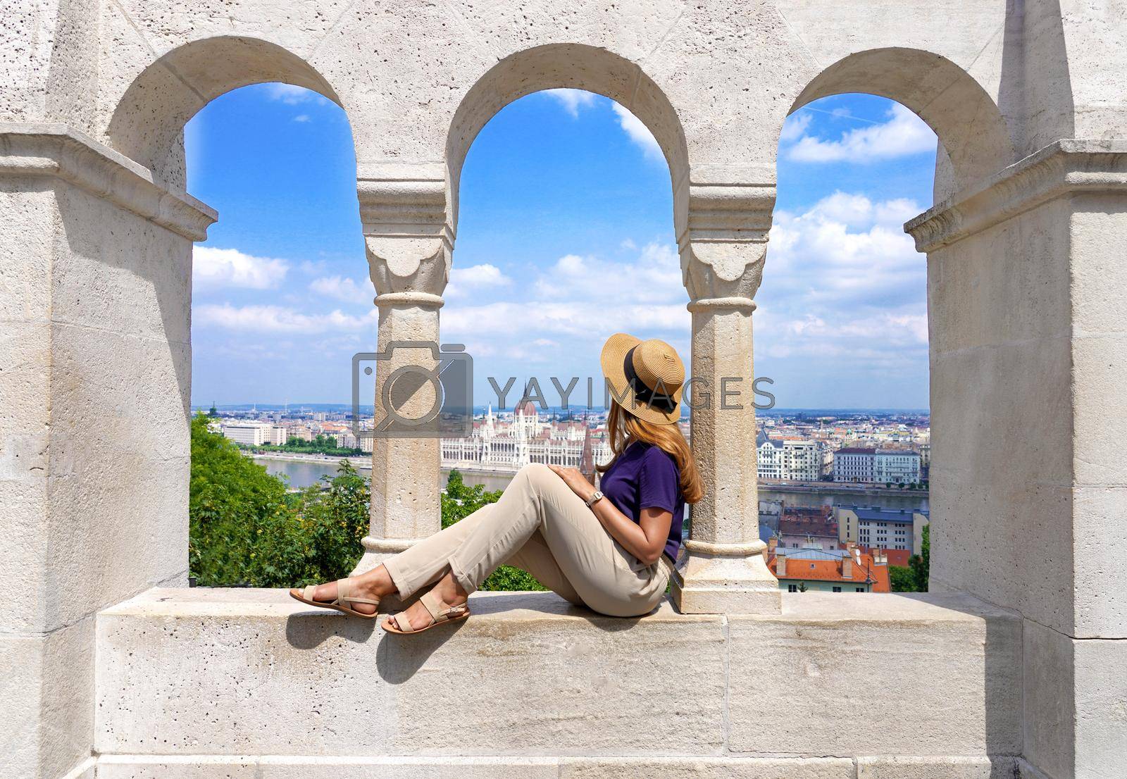 Royalty free image of Beautiful young woman with hat sitting on wall looking at stunning cityscape of Budapest, Hungary by sergio_monti