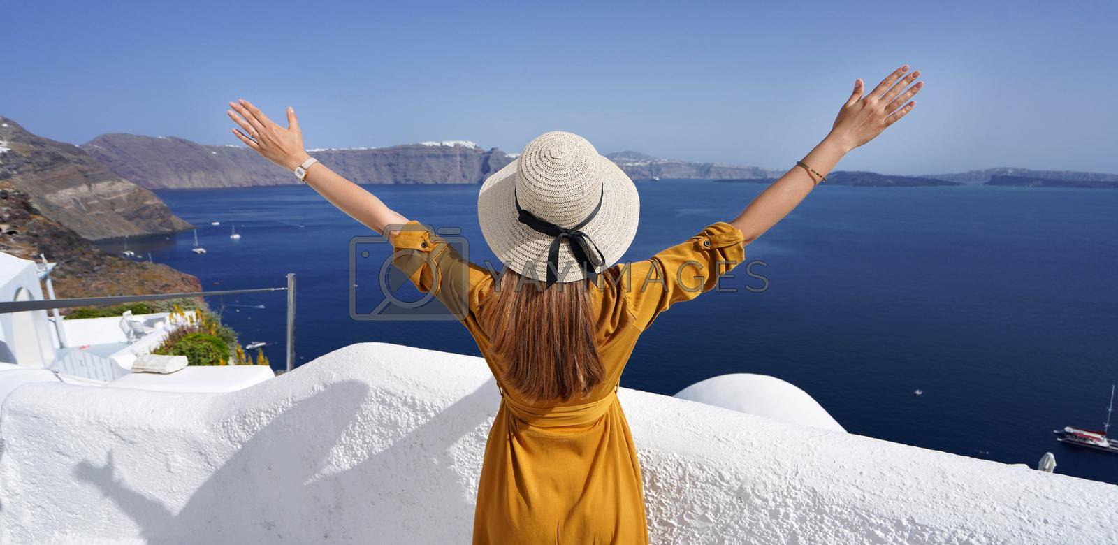Royalty free image of Europe travel vacation woman with arms up looking Santorini Caldera in Greece. Carefree tourist girl in European destination wearing fashion dress and hat. by sergio_monti