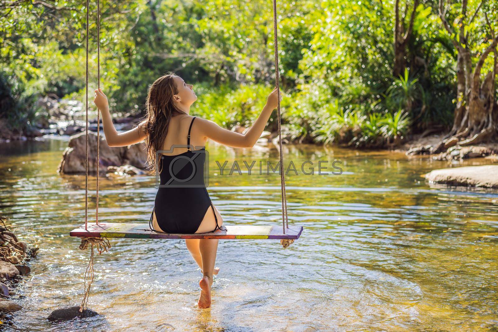 Royalty free image of Beautiful happy girl, young pretty cheerful woman traveler sitting, swinging on a swing tied to a tree above the water, smiling in sunny day. Summer vacation, travel concept by galitskaya