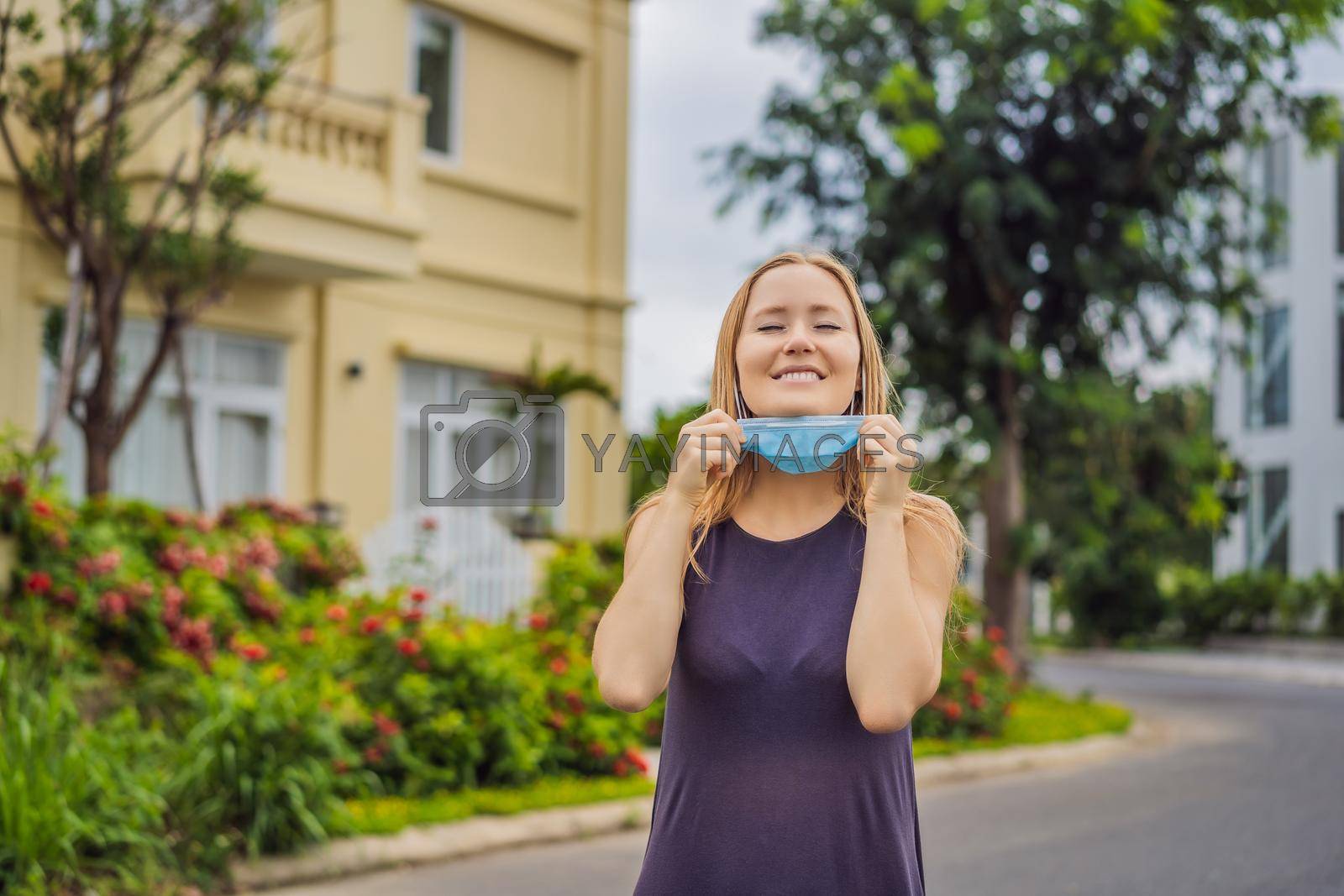 Royalty free image of Quarantine is over concept. Woman taking off mask against the background of small town houses. We are safe. Coronavirus ended. We won. No more quarantine. Breathe deep. Take off the mask. Coronavirus is over by galitskaya
