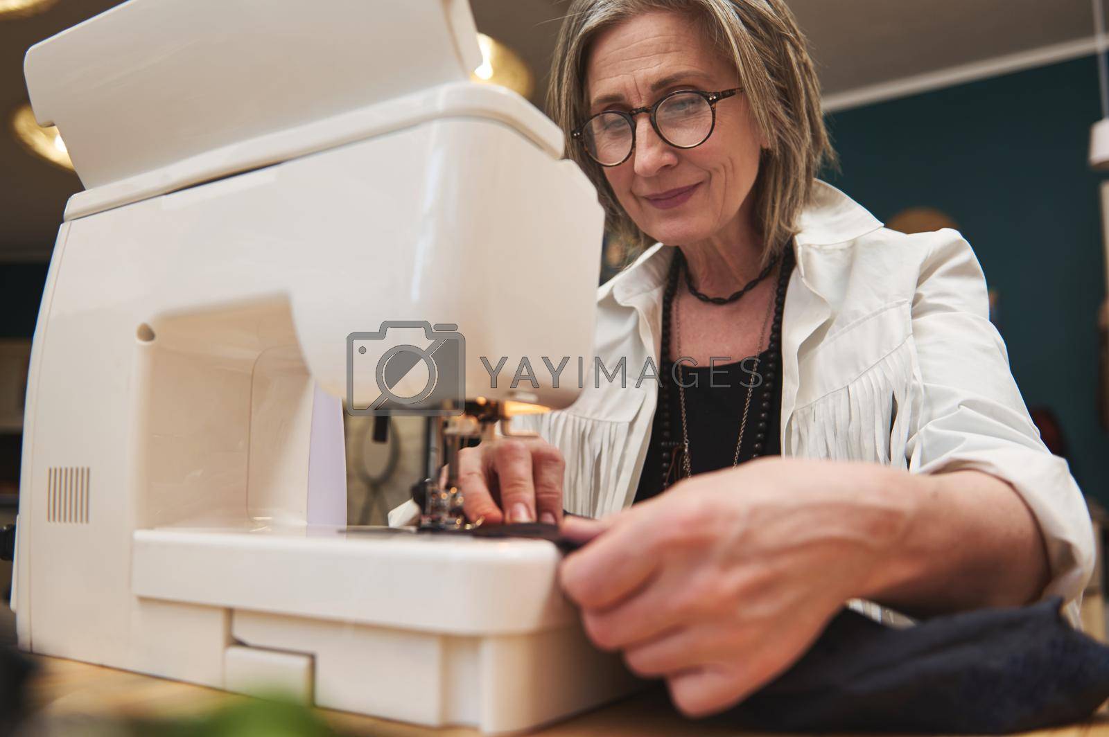 Royalty free image of A fashion designer tailor stitching black cloth on a manufacturing sewing machine in a tailoring atelier. Fashion design concept by artgf
