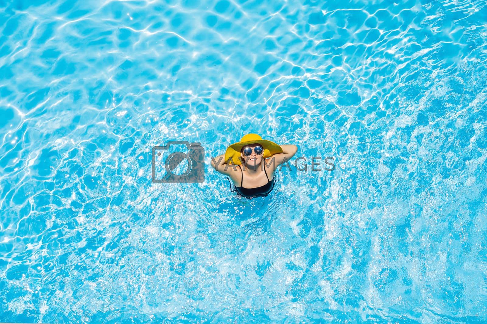Royalty free image of Woman sitting in a swimming pool in a large yellow sunhat by galitskaya