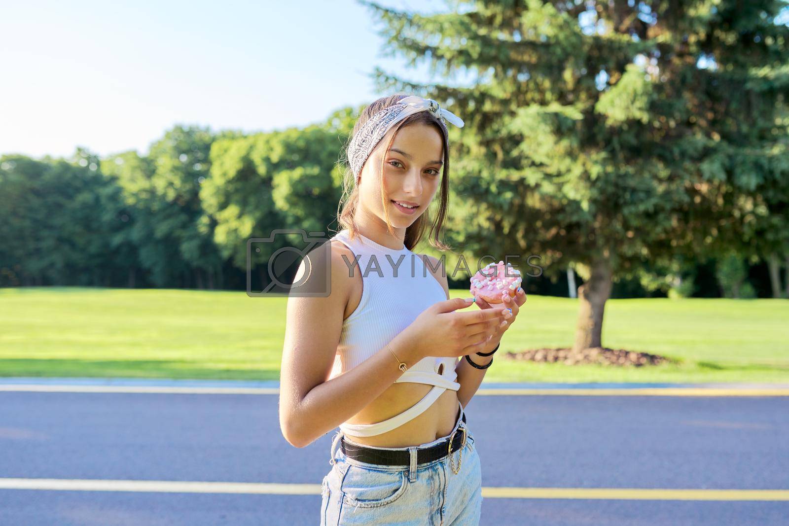 Royalty free image of Portrait of cheerful teenage girl with donut cake, in summer park by VH-studio