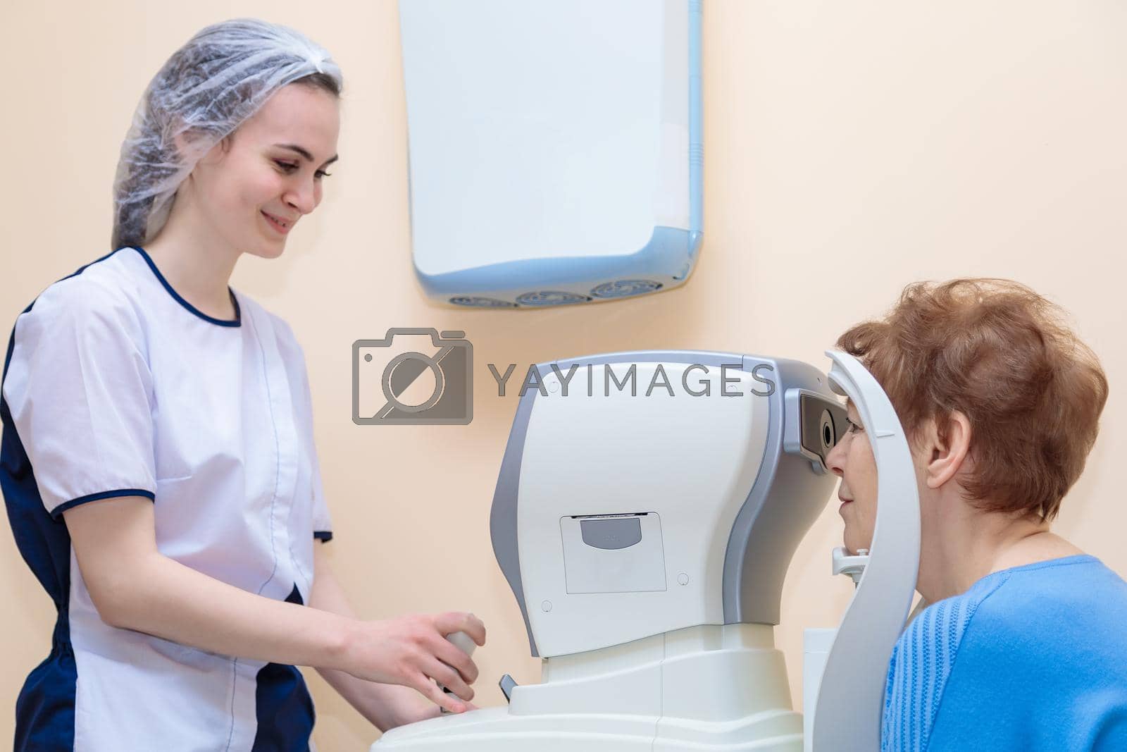 Royalty free image of A girl optometrist examines the eyes of a patient using special modern equipment by Yurich32