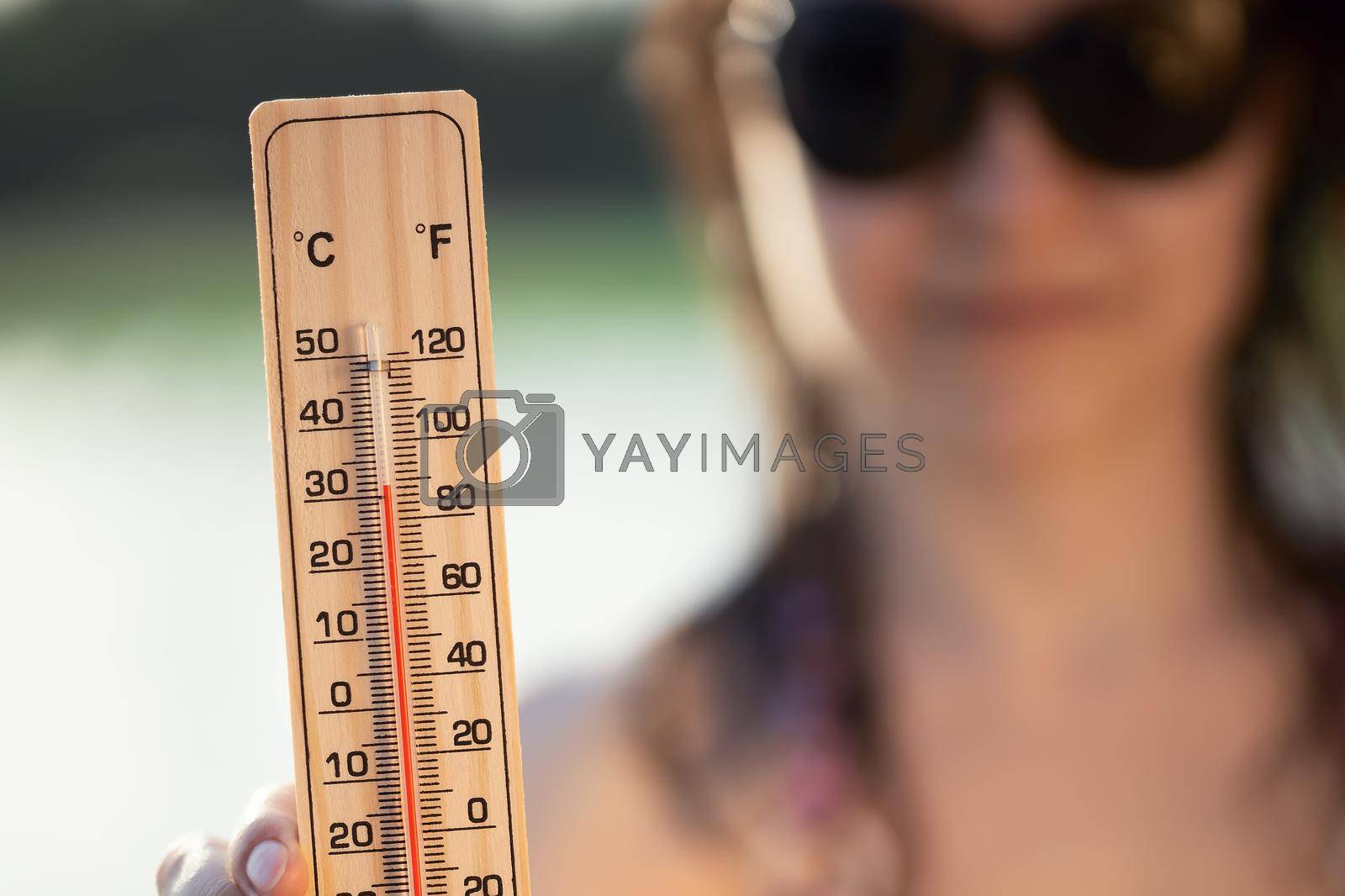 Royalty free image of Beautiful young woman in sunglasses with a thermometer in her hand on the background of the lake. Summer vacation and heat concept, selective focus by galsand