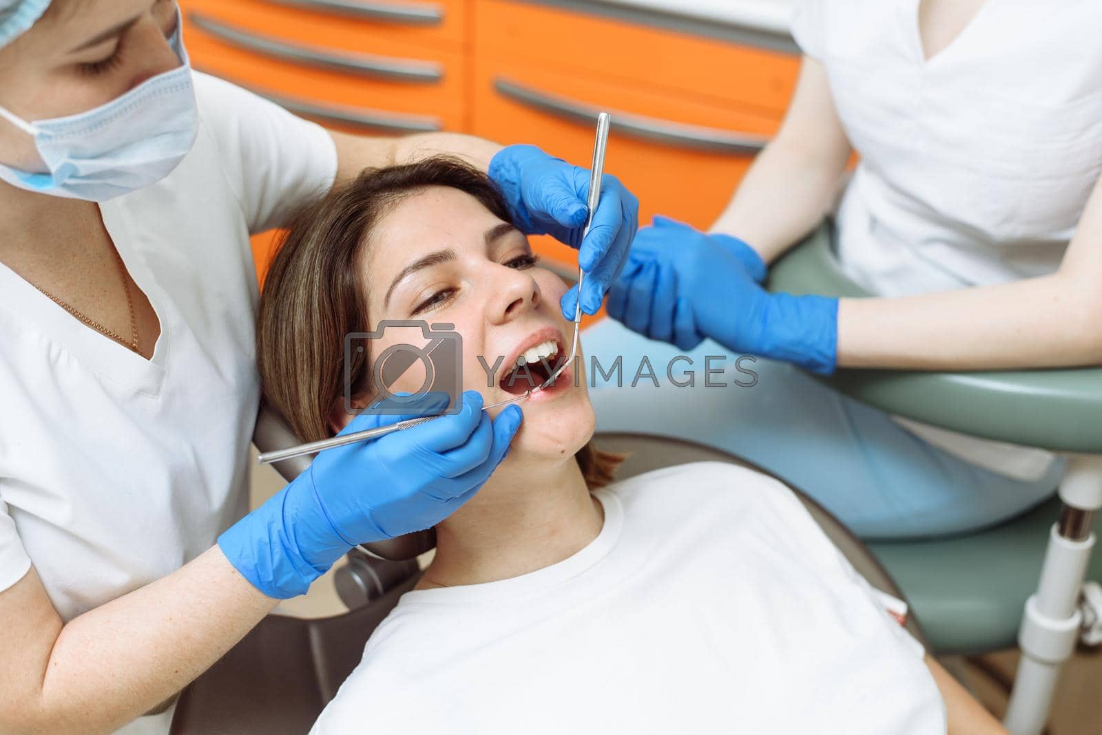 Medical treatment at the dentist office. Female dentist and assistant in dental office examining young woman with tools in dental clinic.