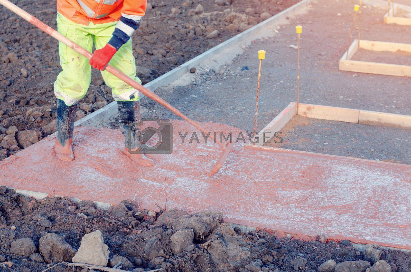 Royalty free image of Concreter spreading poured concrete with a rake or spazzle A construction worker is levelling tinted concrete in formwork by Iryna_Melnyk