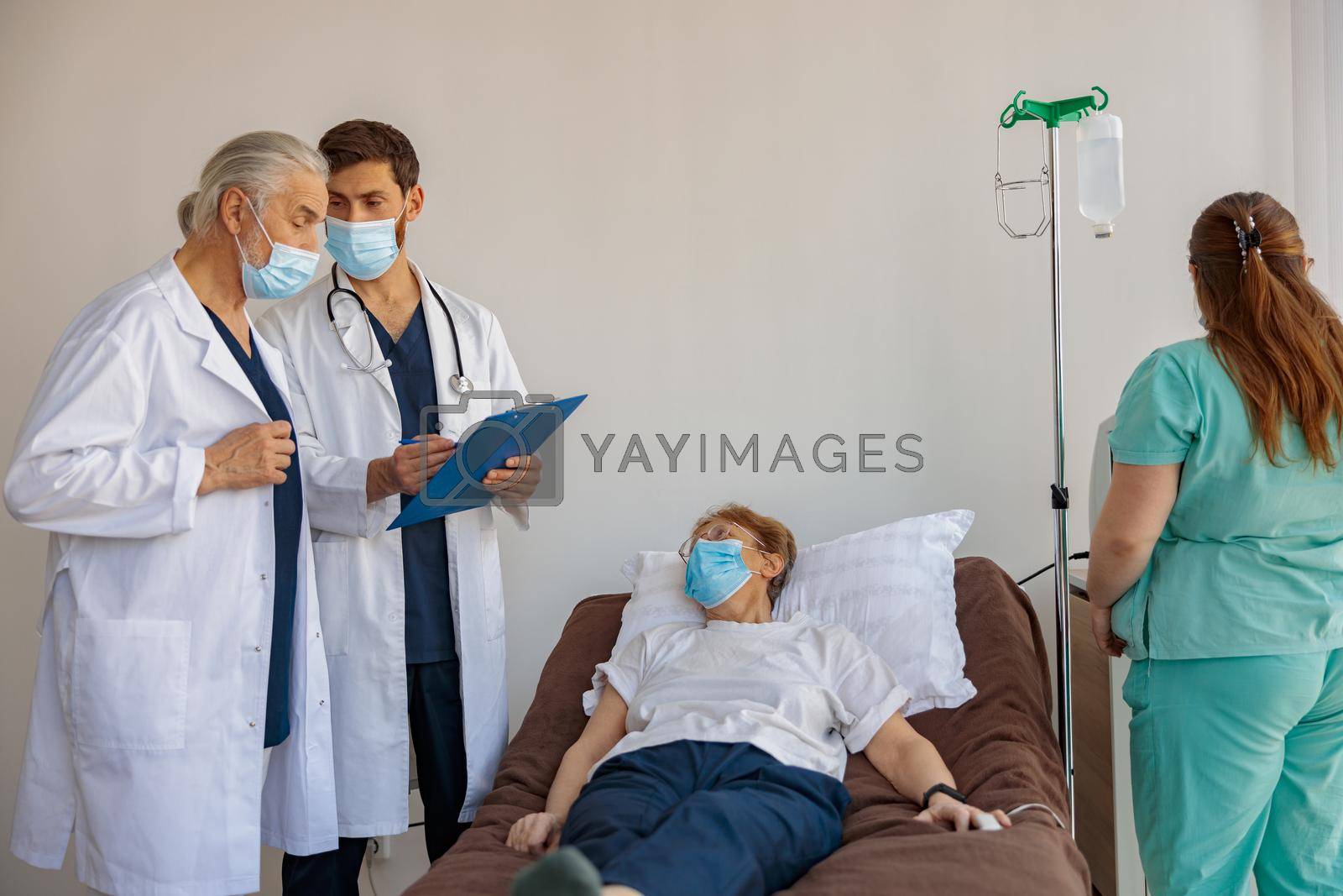 Royalty free image of Professional doctors discuss over patient's diagnosis standing in hospital ward by Yaroslav_astakhov