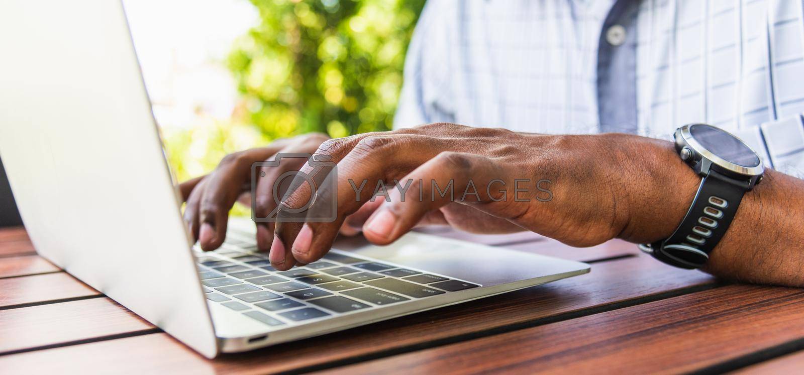 Happy Asian black businessman person or office worker wear face mask protect sitting on desk work from home using laptop computer typing keyboard and connect networking online at the coffee cafe shop