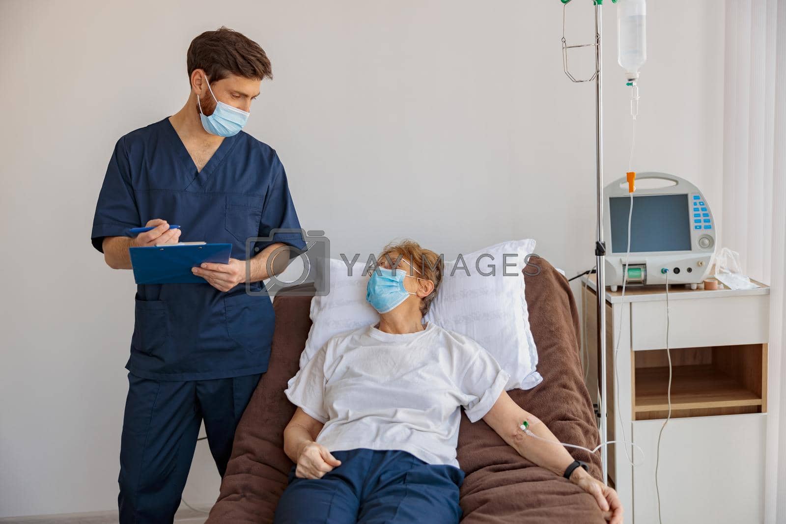 Royalty free image of Doctor in mask writing down patient symptoms in hospital ward during Covid-19 epidemic by Yaroslav_astakhov