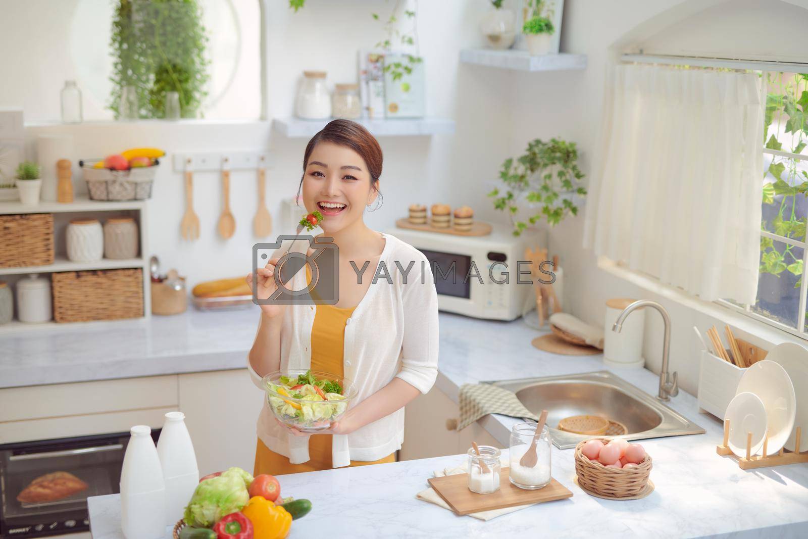 Royalty free image of Beautiful Smiling Woman Eating Fresh Organic Vegetarian Salad In Modern Kitchen. by makidotvn
