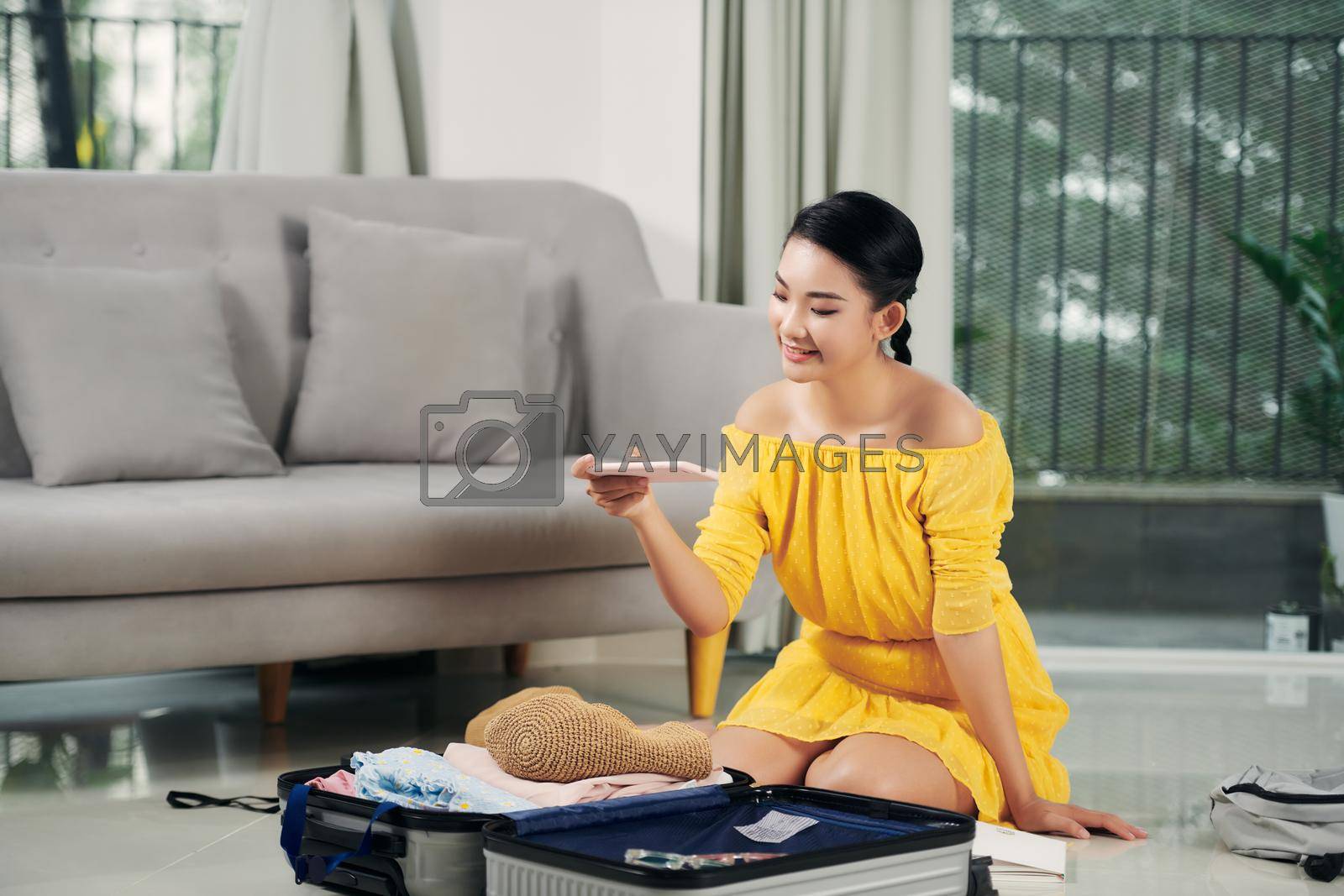 Royalty free image of Young woman traveler using smartphone and packing her suitcase preparing for travel on summer vacation by makidotvn
