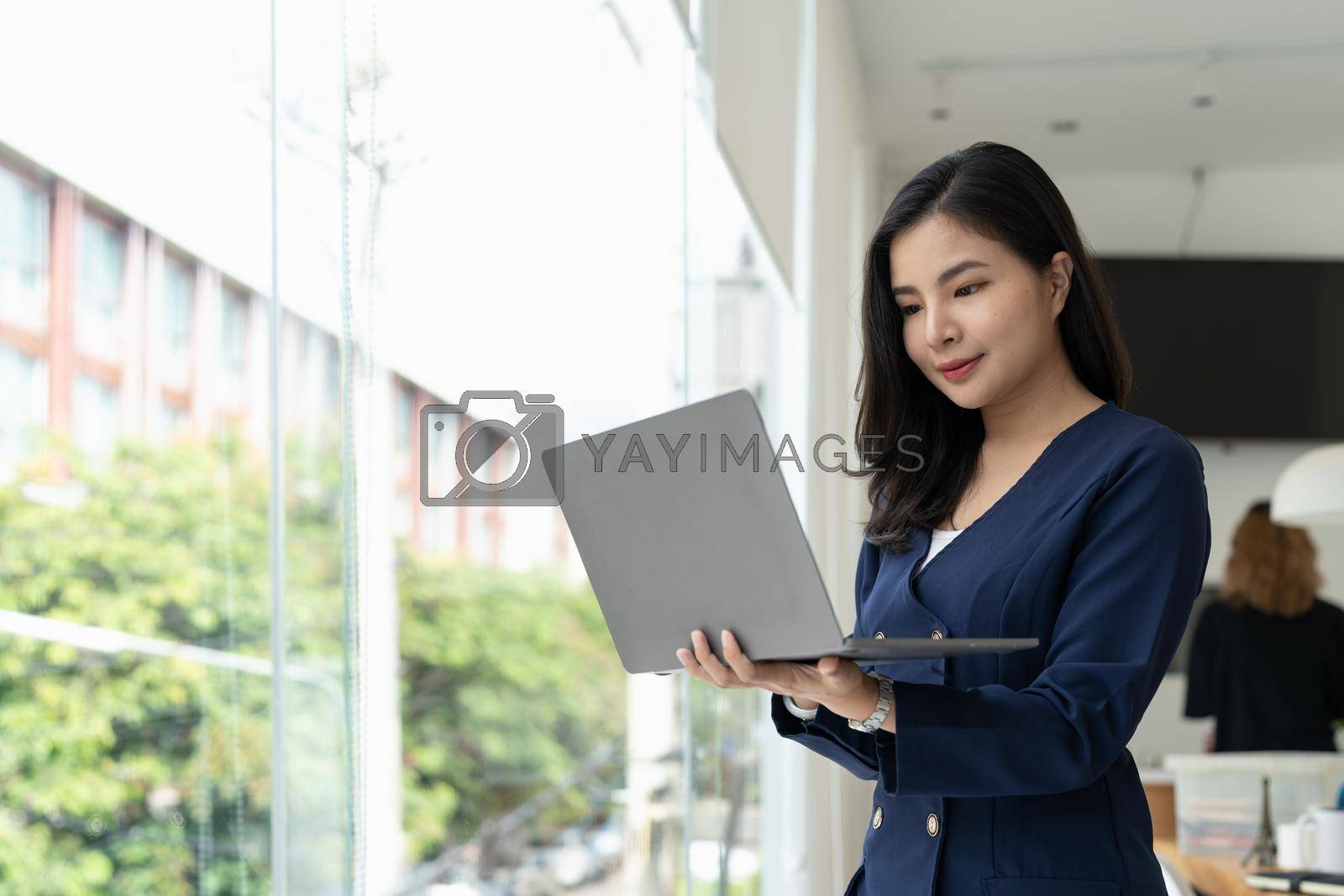Royalty free image of Asian businesswoman standing in modern office and using laptop computer by nateemee