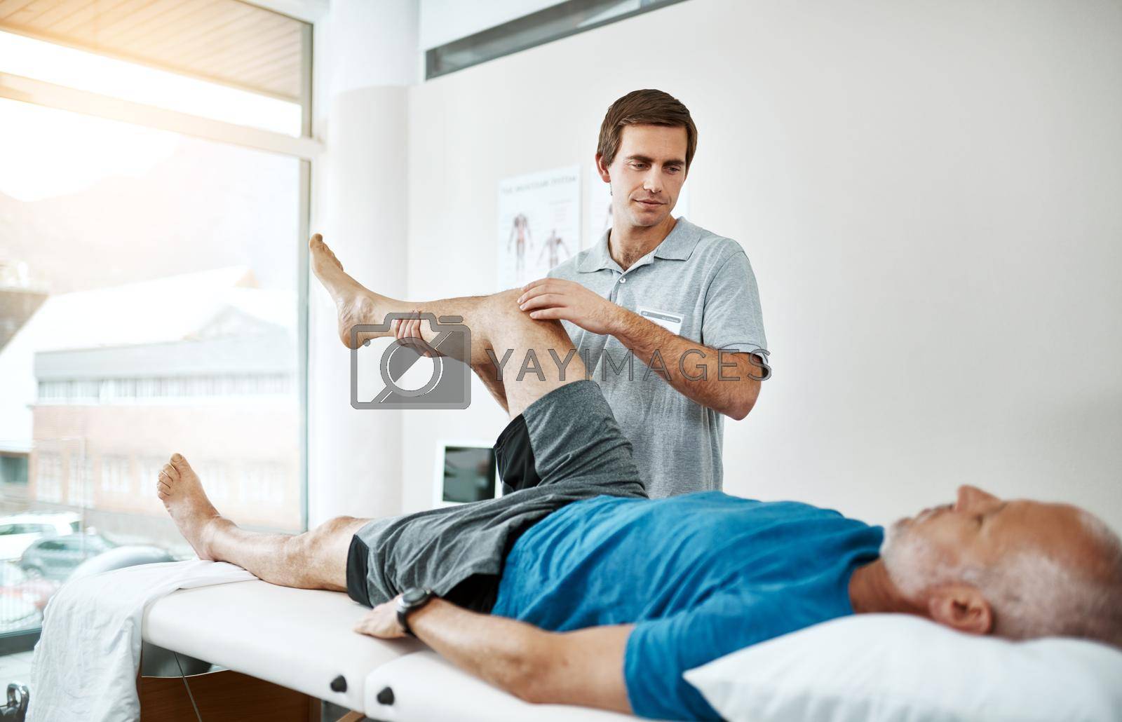 Royalty free image of Client health is his only concern. Shot of a young male physiotherapist helping a client with leg exercises whos lying on a bed. by YuriArcurs