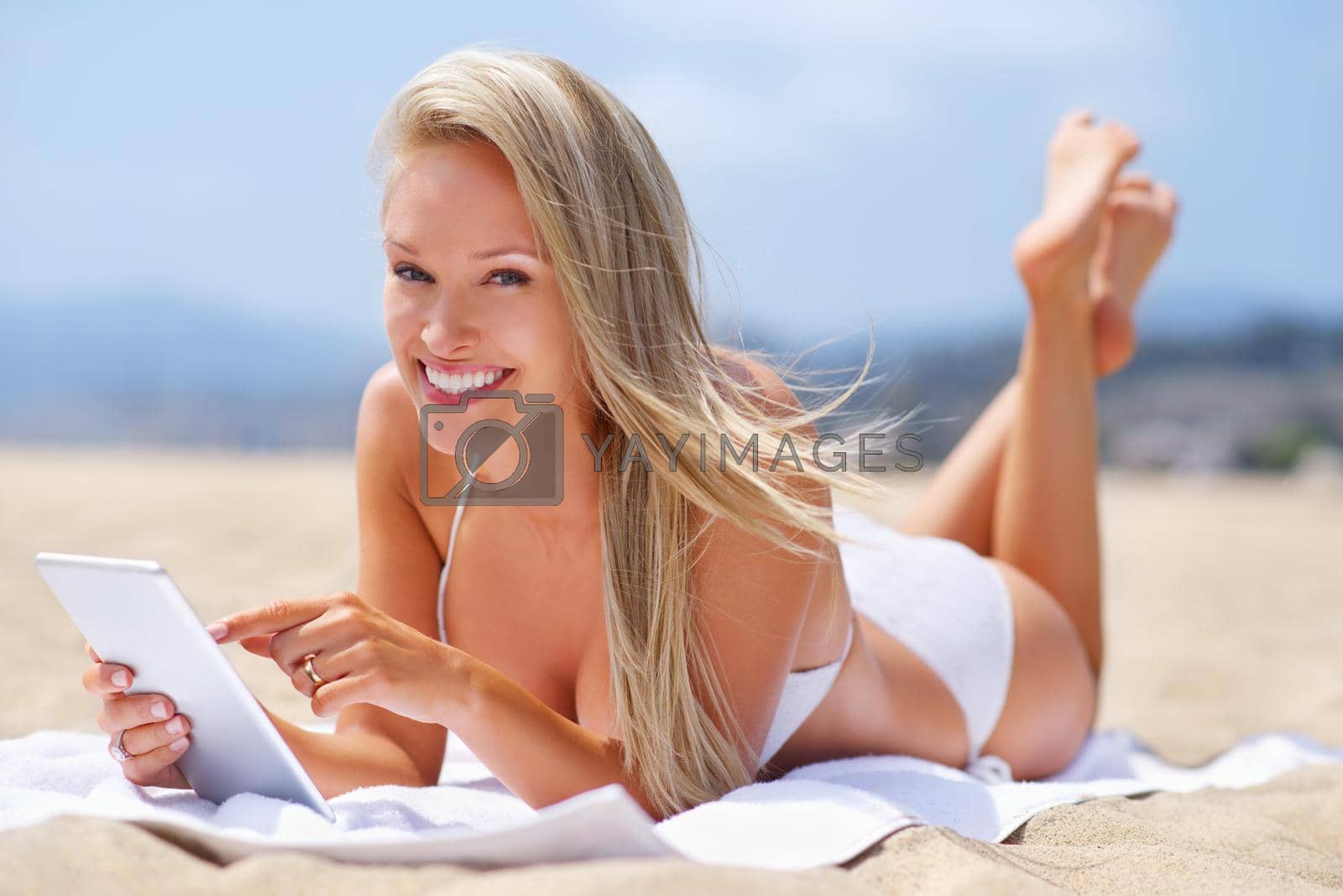 Royalty free image of Status update...catching a tan and feeling great. A tanned woman relaxing on the beach while using her tablet. by YuriArcurs