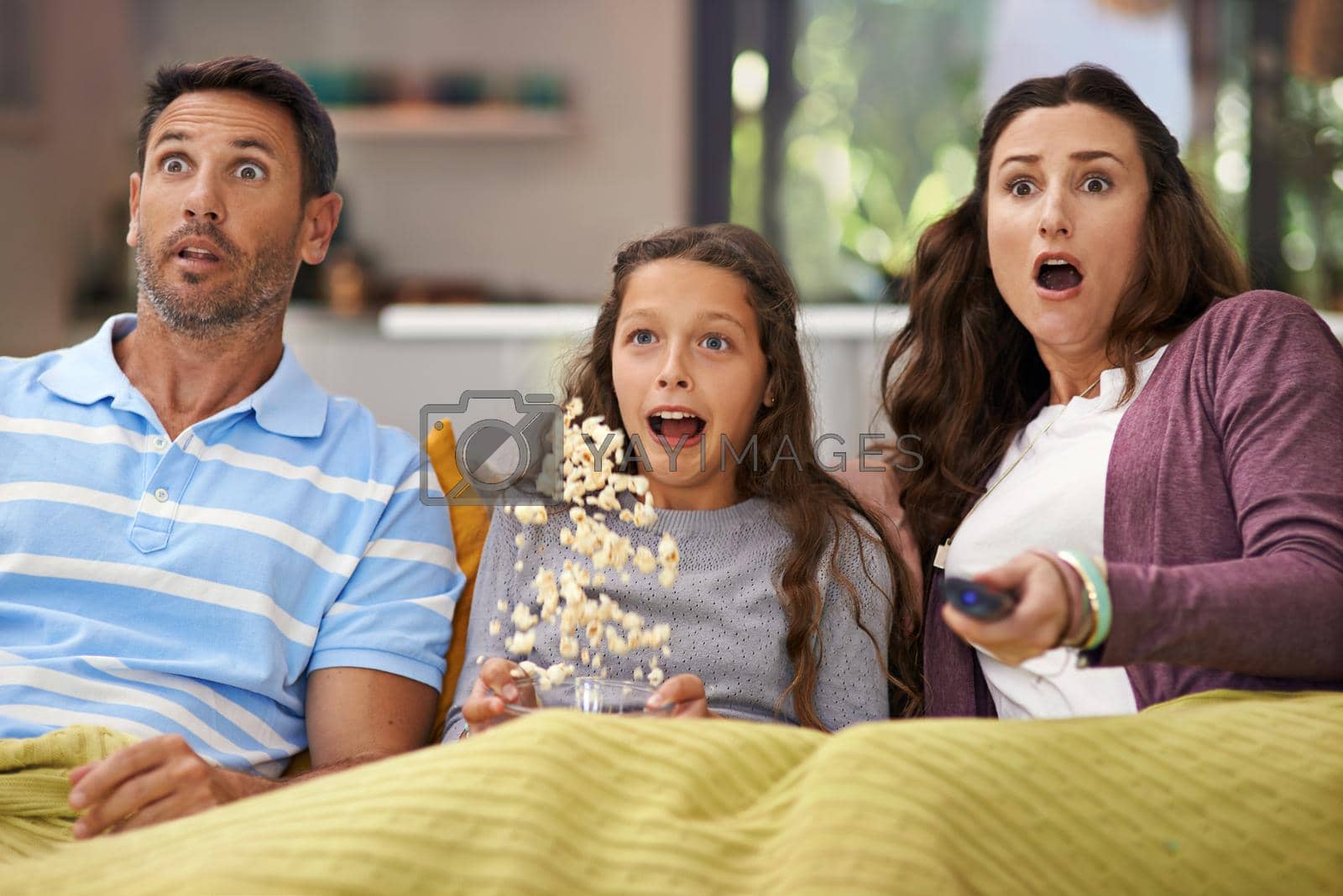 Royalty free image of They love scary movies. Shot of a family sitting on their living room sofa watching a movie and eating popcorn. by YuriArcurs