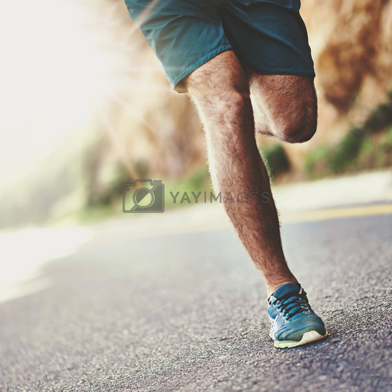 Royalty free image of Time for these feet to burn up the pavement. Low angle shot of a mans legs running along a road. by YuriArcurs