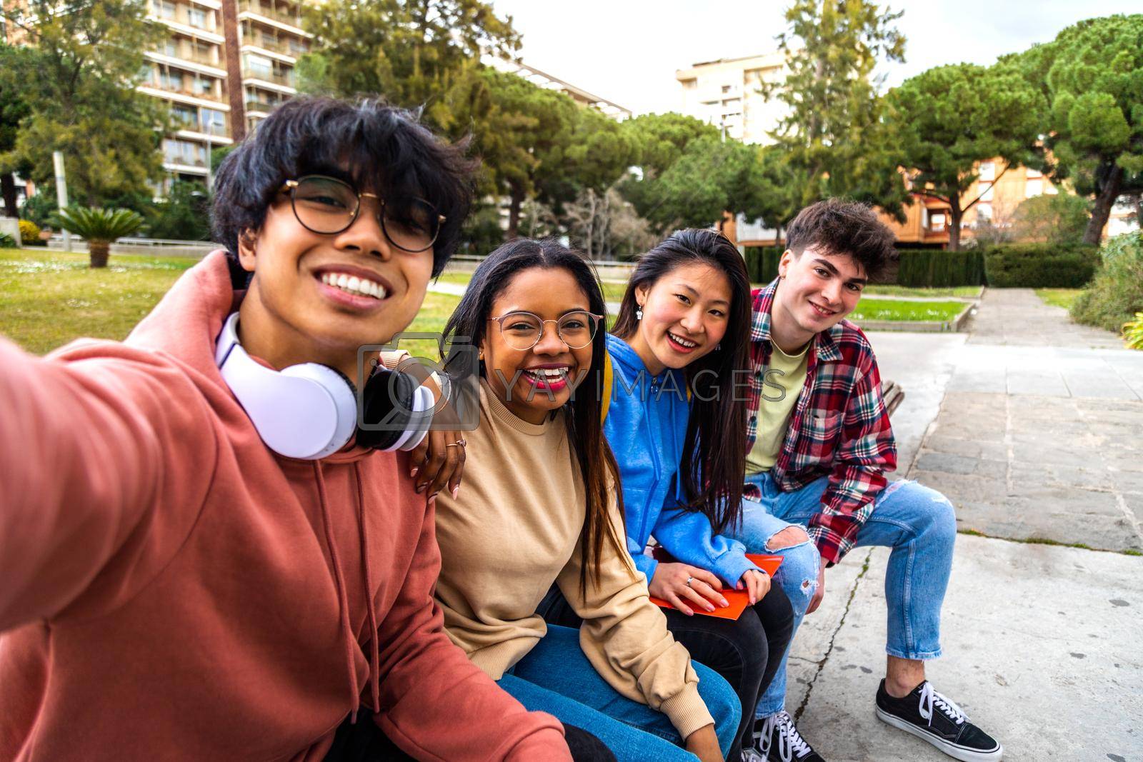 Group of multiracial college student friends taking selfie with phone outside. Students laughing and having fun in park. Youth lifestyle concept.