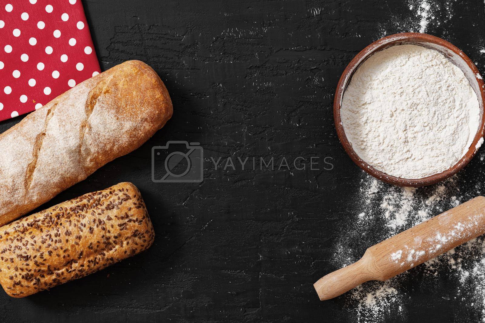 Royalty free image of Fresh bread with bowl of flour on dark background by Fabrikasimf