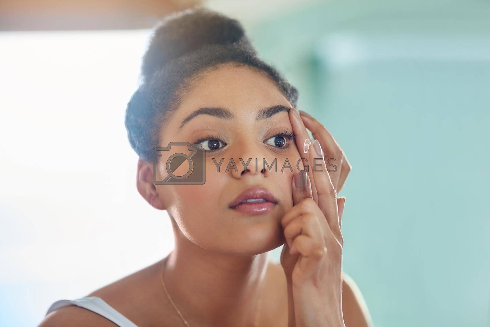 Royalty free image of Helping her live the life she envisions. Shot of an attractive young woman putting in her contact lenses at home. by YuriArcurs