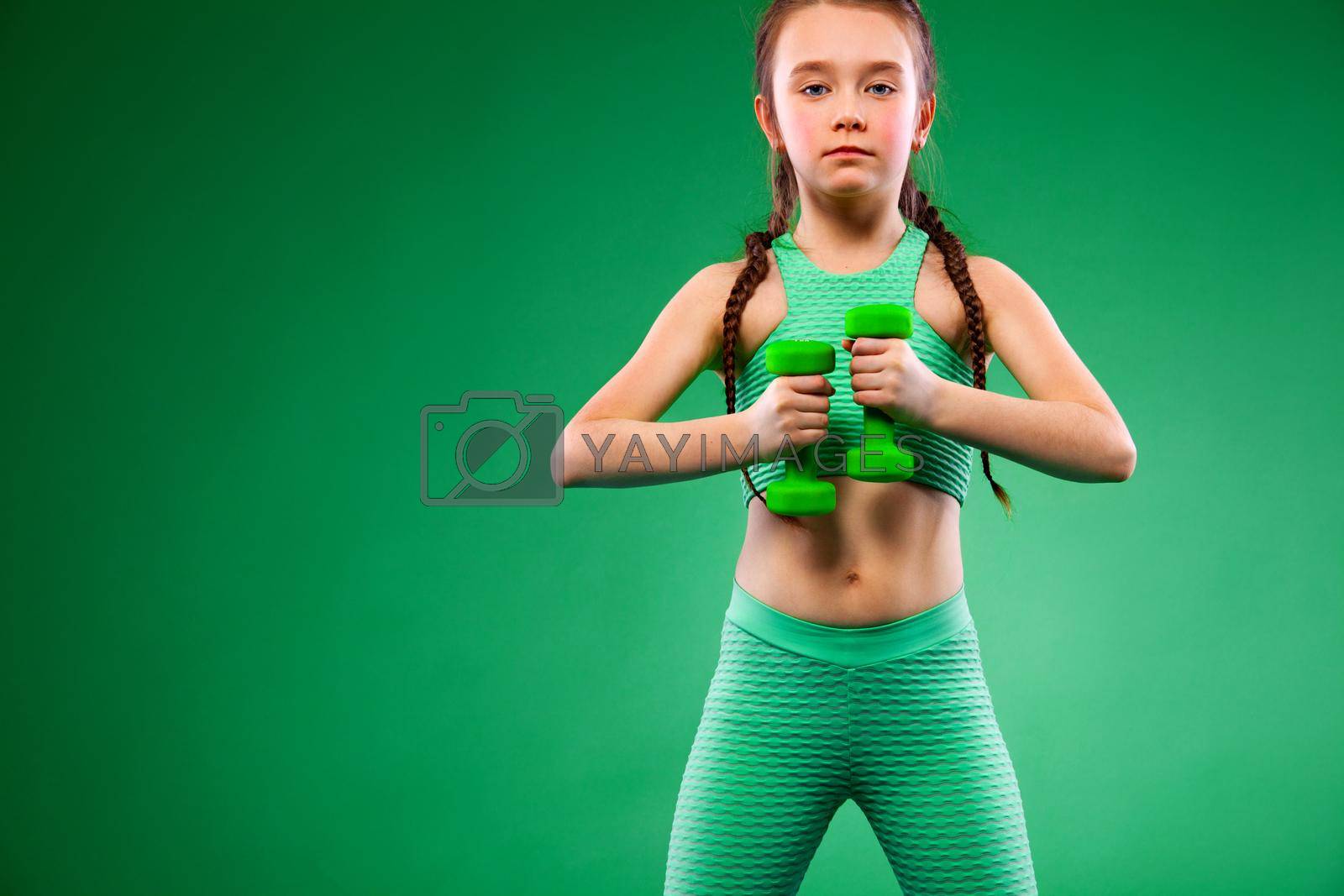 Royalty free image of Kid girl doing fitness exercises with dumbbells on green background by MikeOrlov