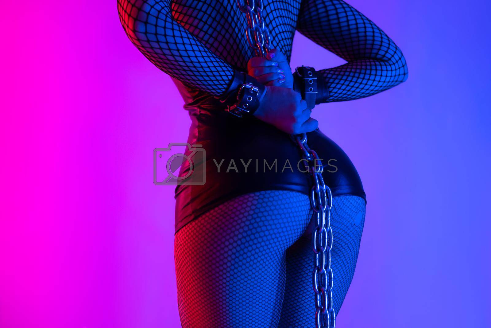Royalty free image of sexy buttocks close-up of a girl in a latex bdsm mistress costume with torn tights in neon light by Rotozey