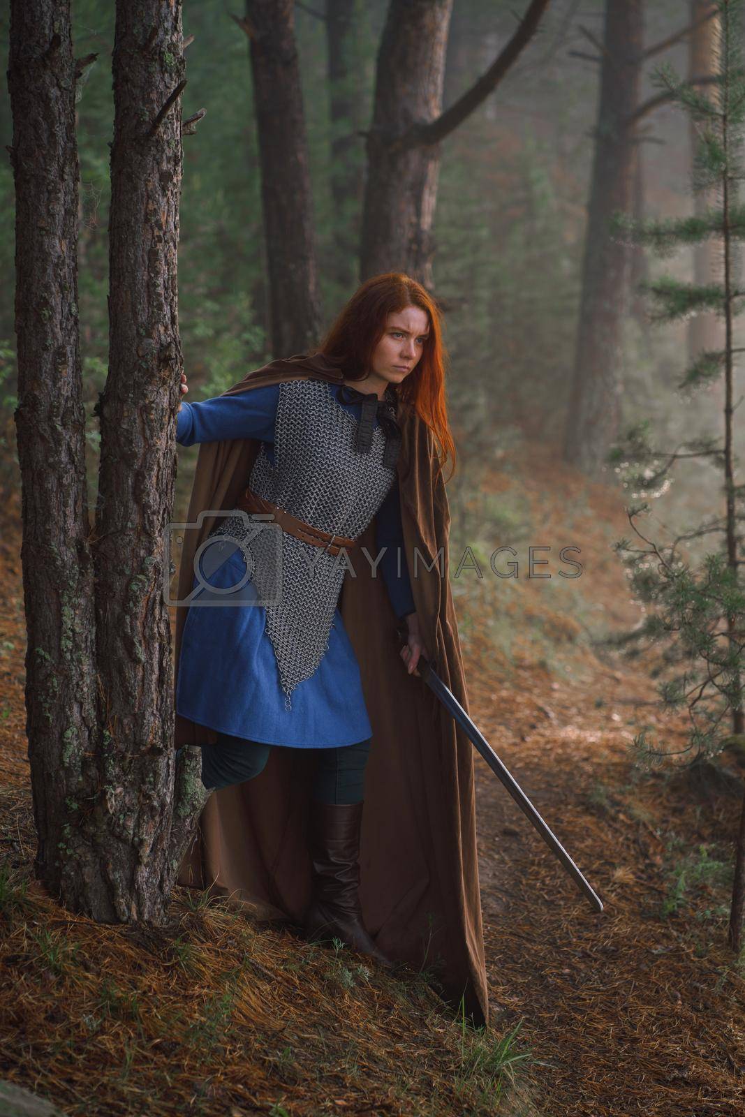 Royalty free image of Red-haired girl in armor and raincoat in forest. Historical concept by fotokvadrat