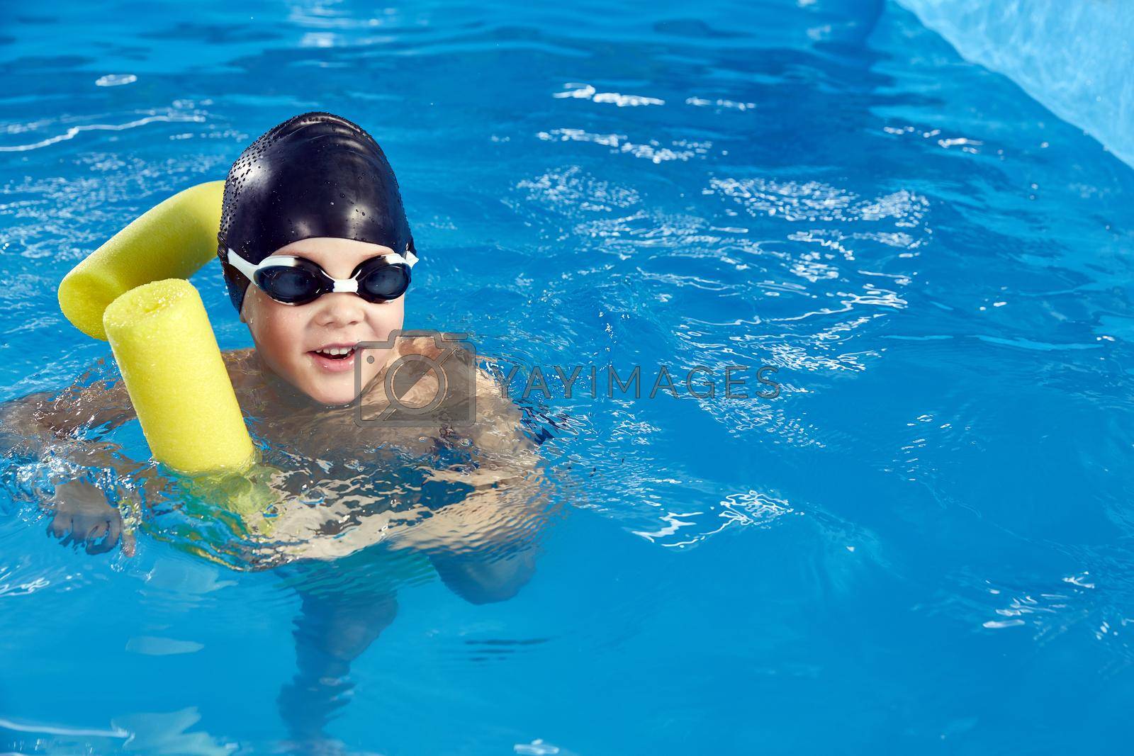 Royalty free image of Preschool boy learning to swim in pool with foam noodle by Mariakray