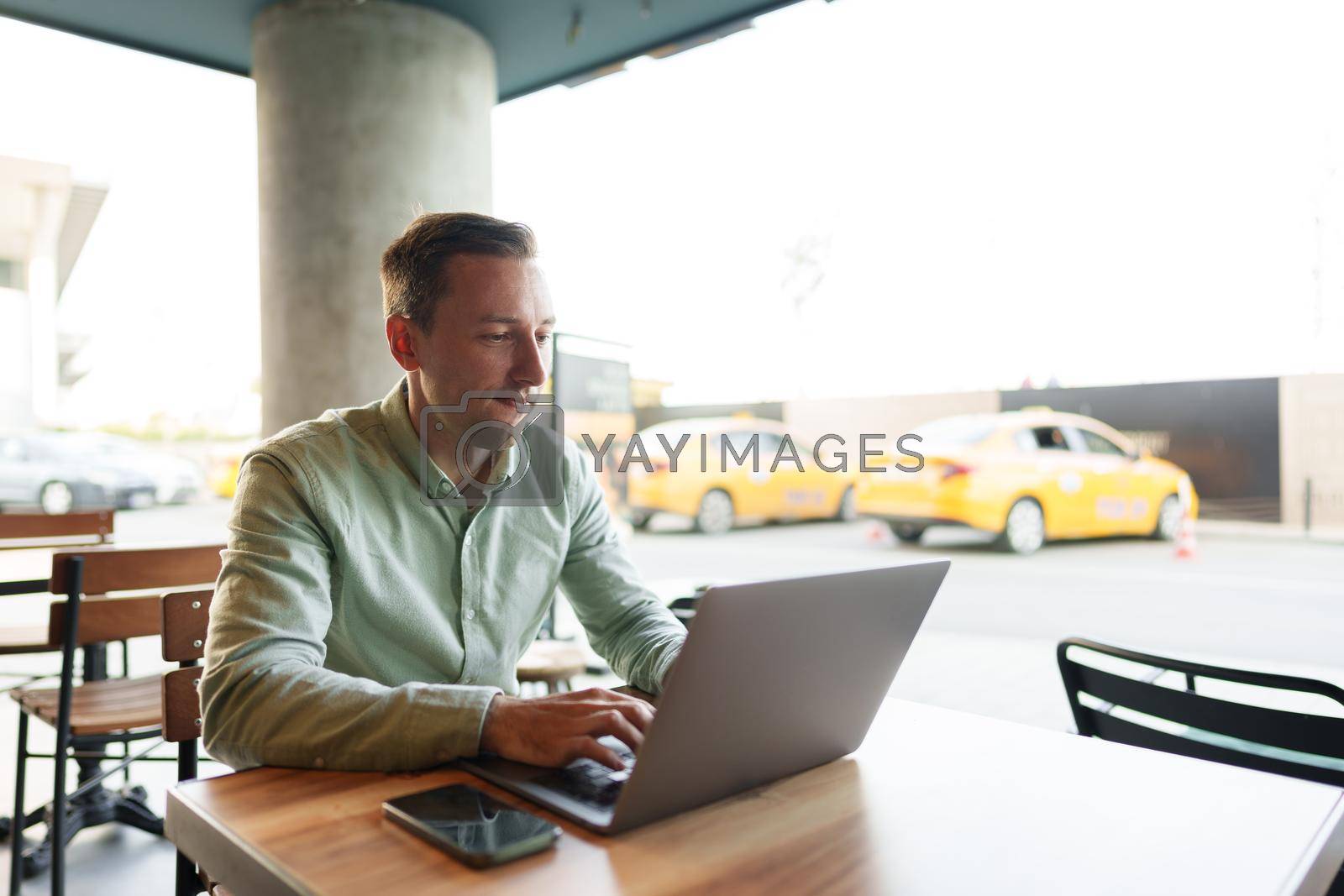 Royalty free image of Young businessman sitting in cafe working with laptop computer by Fabrikasimf