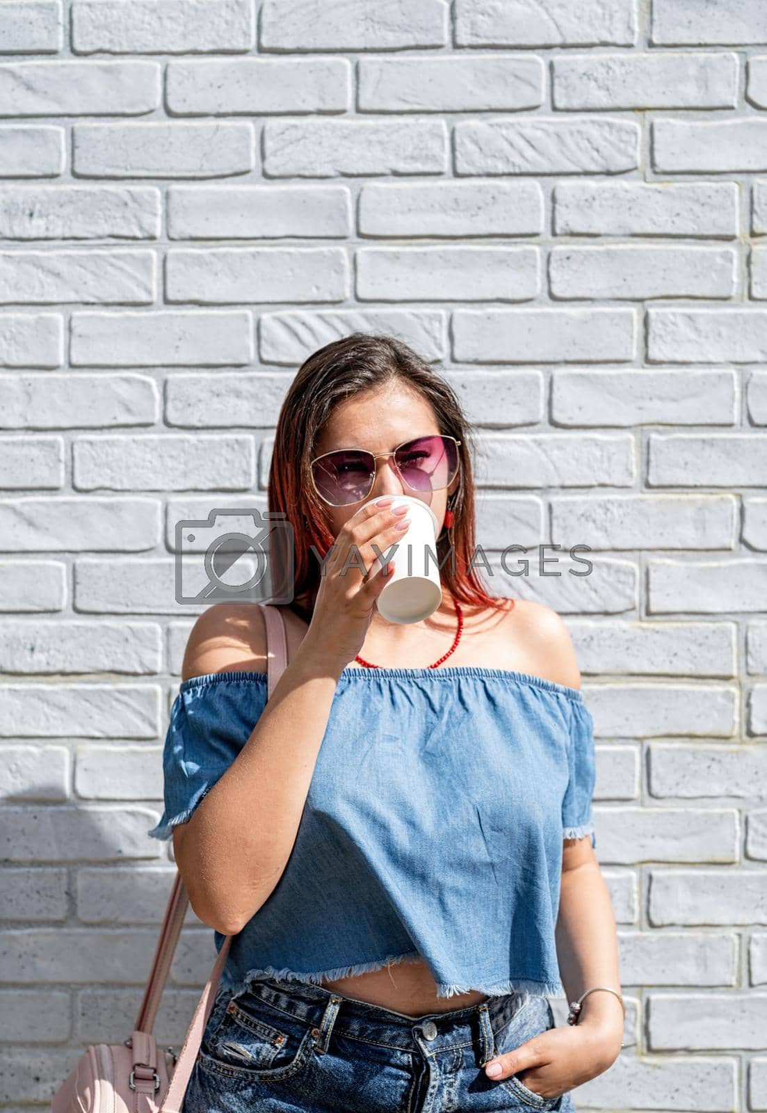 Royalty free image of Stylish millennial woman drinking coffee at stree in summer, white brick wall background by Desperada
