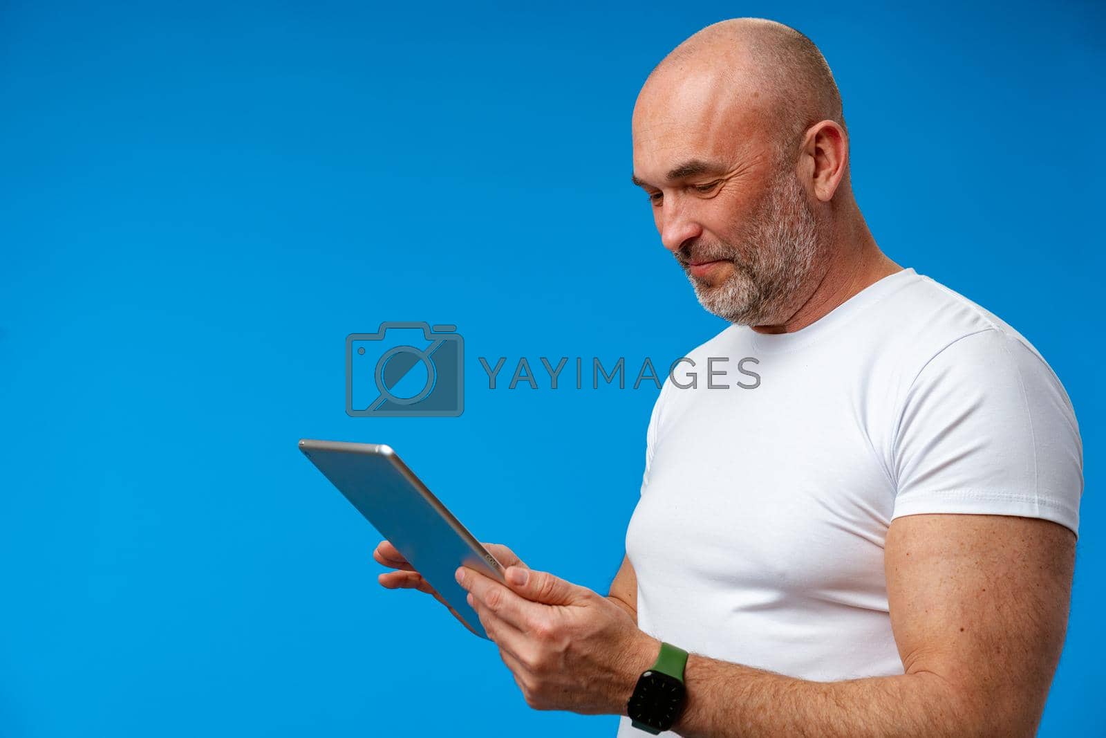 Royalty free image of Handsome middle age man with digital tablet against blue background by Fabrikasimf