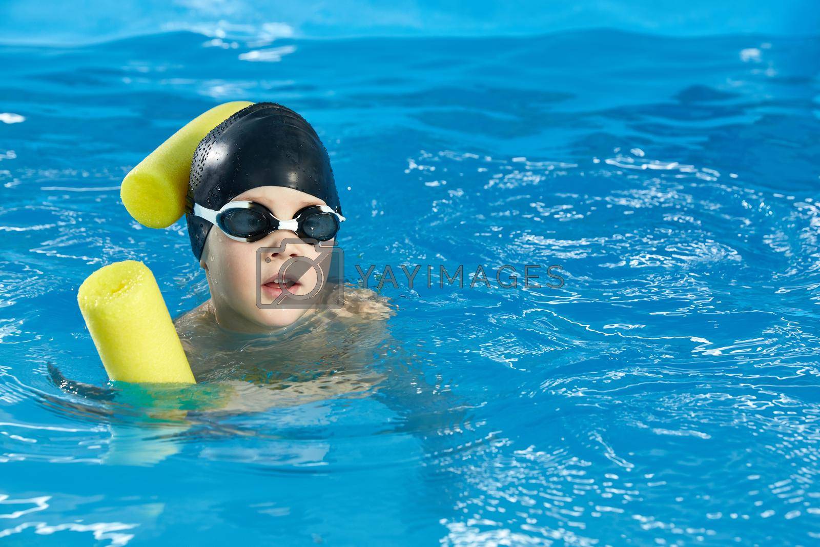 Royalty free image of Preschool boy learning to swim in pool with foam noodle by Mariakray